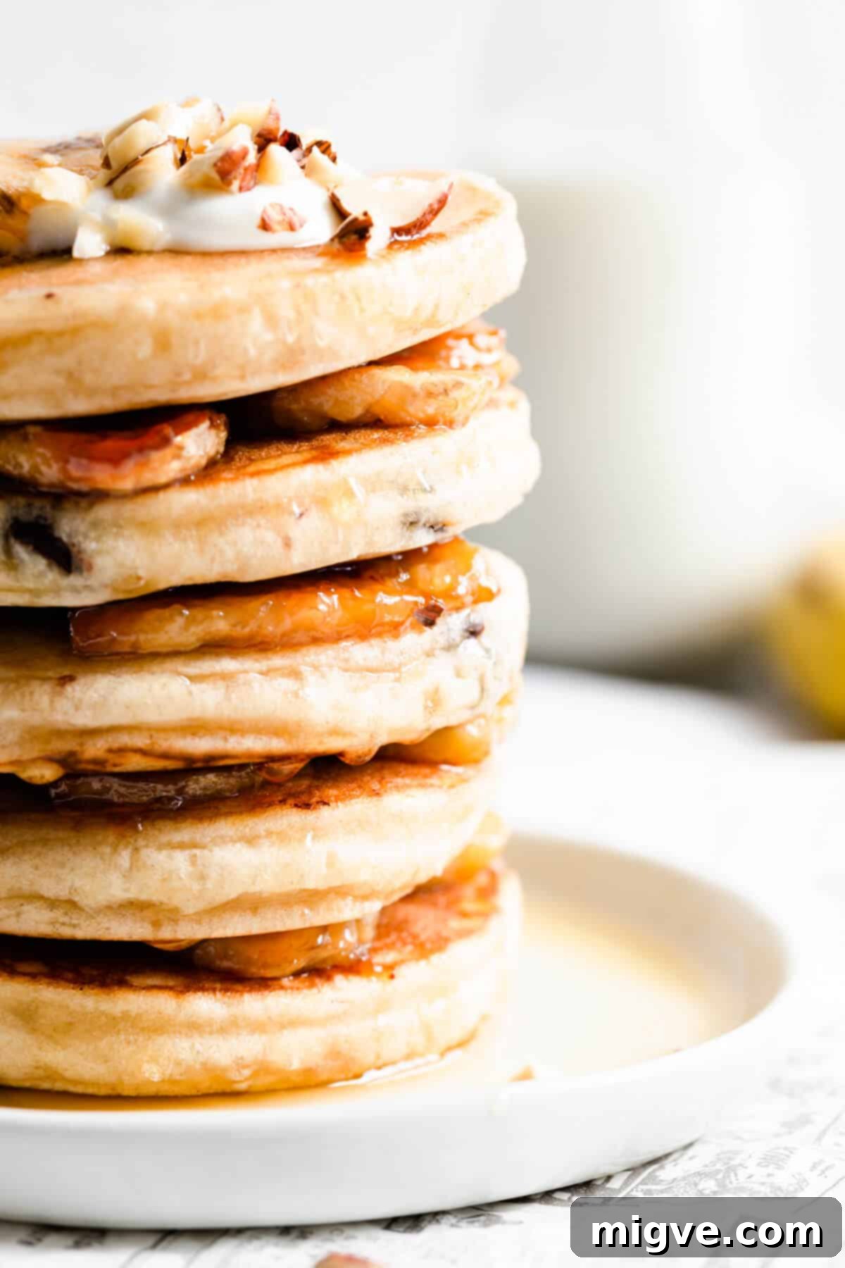 Caramelized Banana Hazelnut Stack 13 Side close-up of a stack of pancakes topped generously with creamy vegan yogurt and garnished with fruit