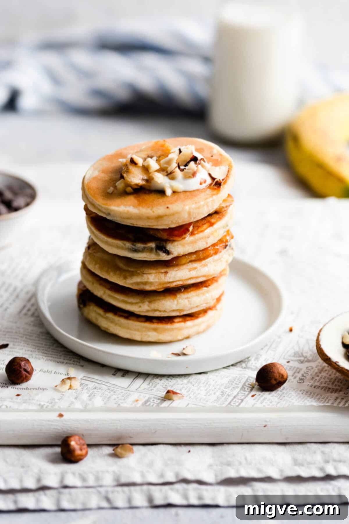 Caramelized Banana Hazelnut Stack 3 Side view of a stack of five thick, fluffy pancakes topped with chopped hazelnuts