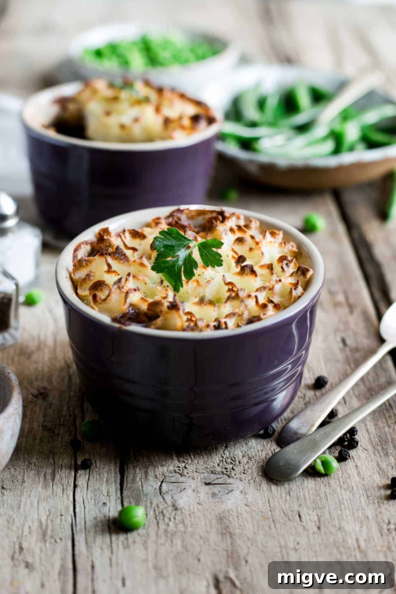 A mini lentil shepherd's pie, freshly baked, served alongside a small portion of green peas, showcasing a complete and appealing meal.