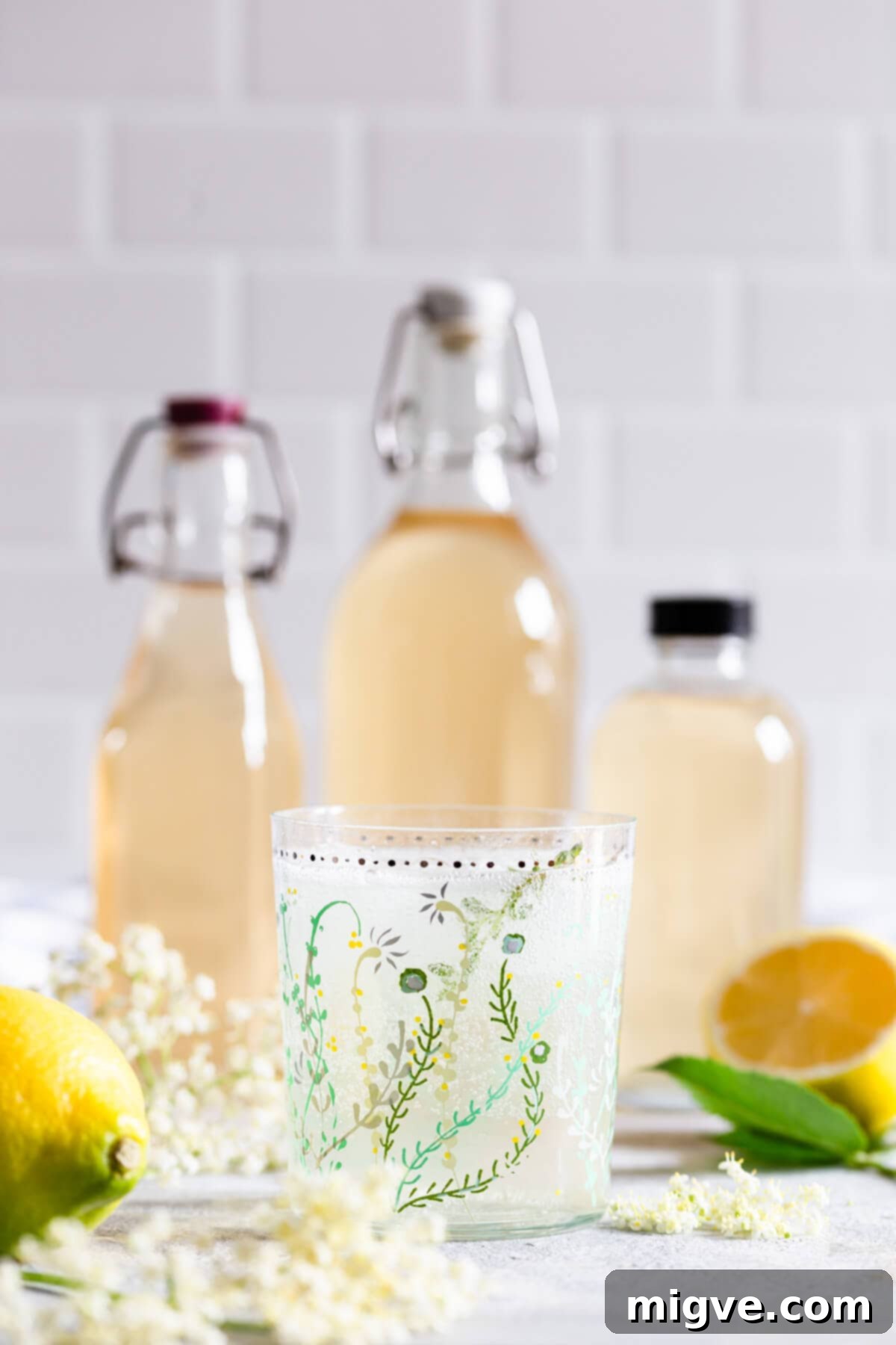 straight ahead view of a glass with fizzy elderflower cordial and cordial bottles at the back