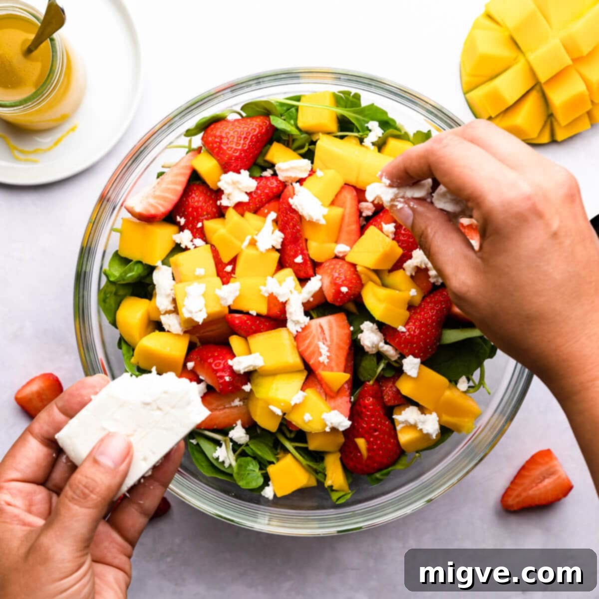overhead photo showing feta cheese being crumbled into a salad bowl