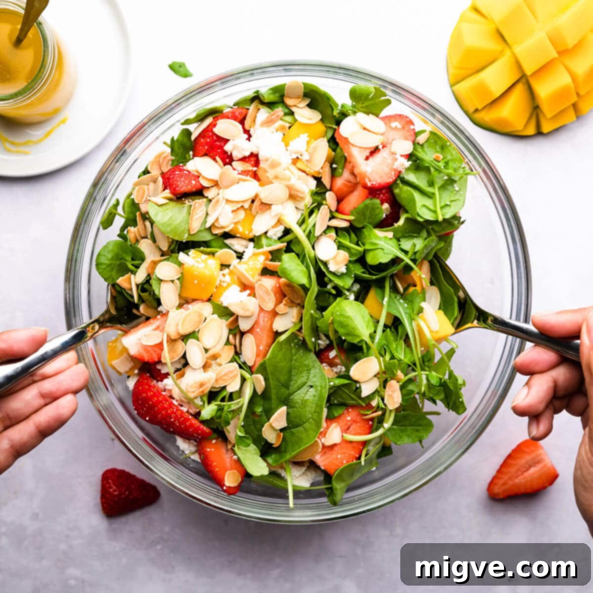 overhead photo showing salad ingredients being mixed in a glass bowl