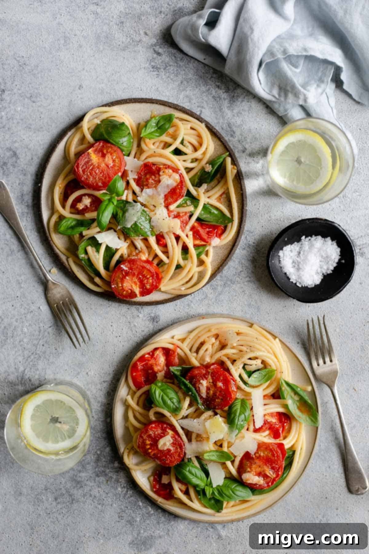 Two plates of bucatini pasta with oven roasted tomatoes and fresh basil, garnished with Parmesan cheese - an easy weeknight recipe