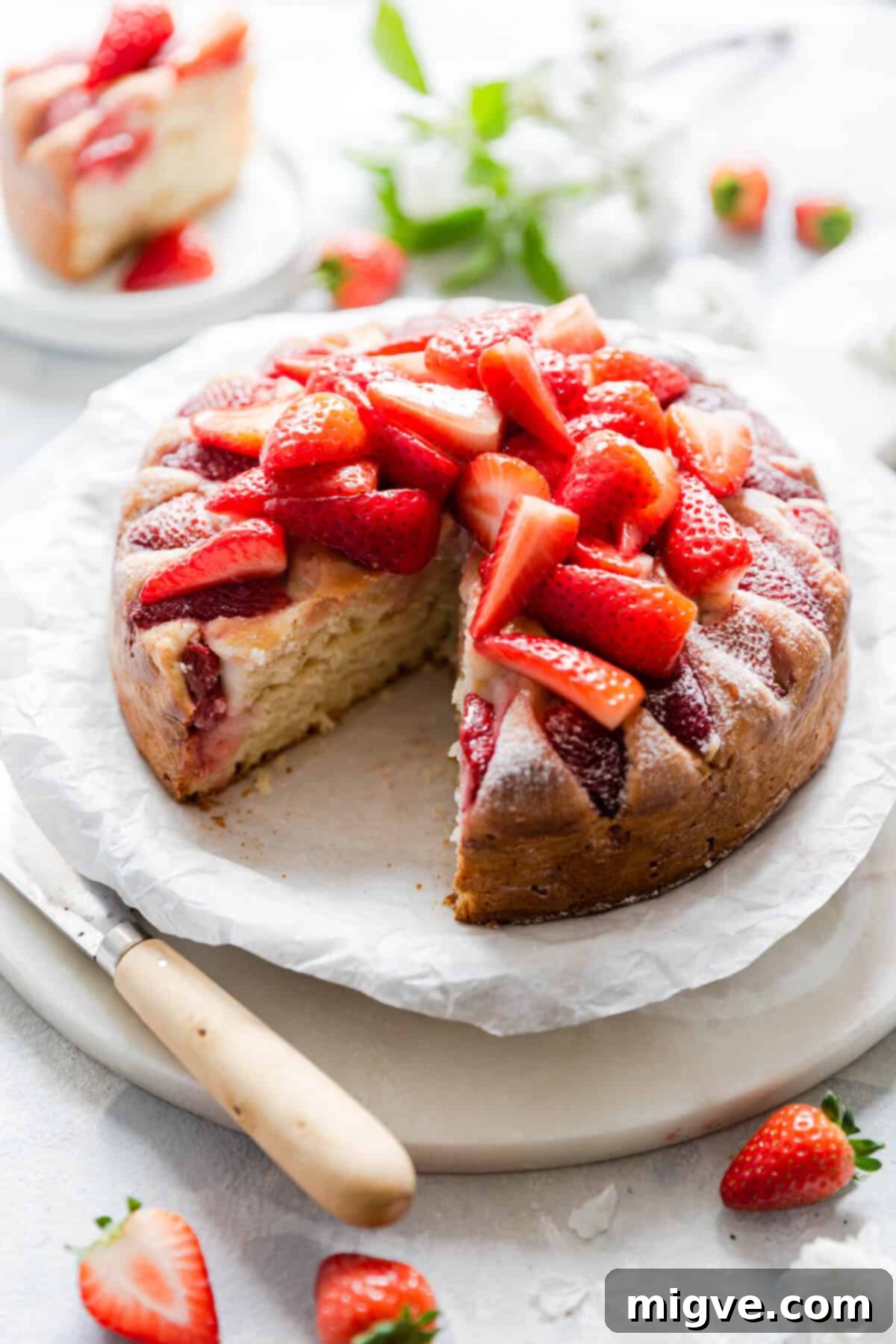 Top-side angle of a fresh strawberry yogurt cake with a slice cut out, showing the moist interior and a dollop of cream on the side.