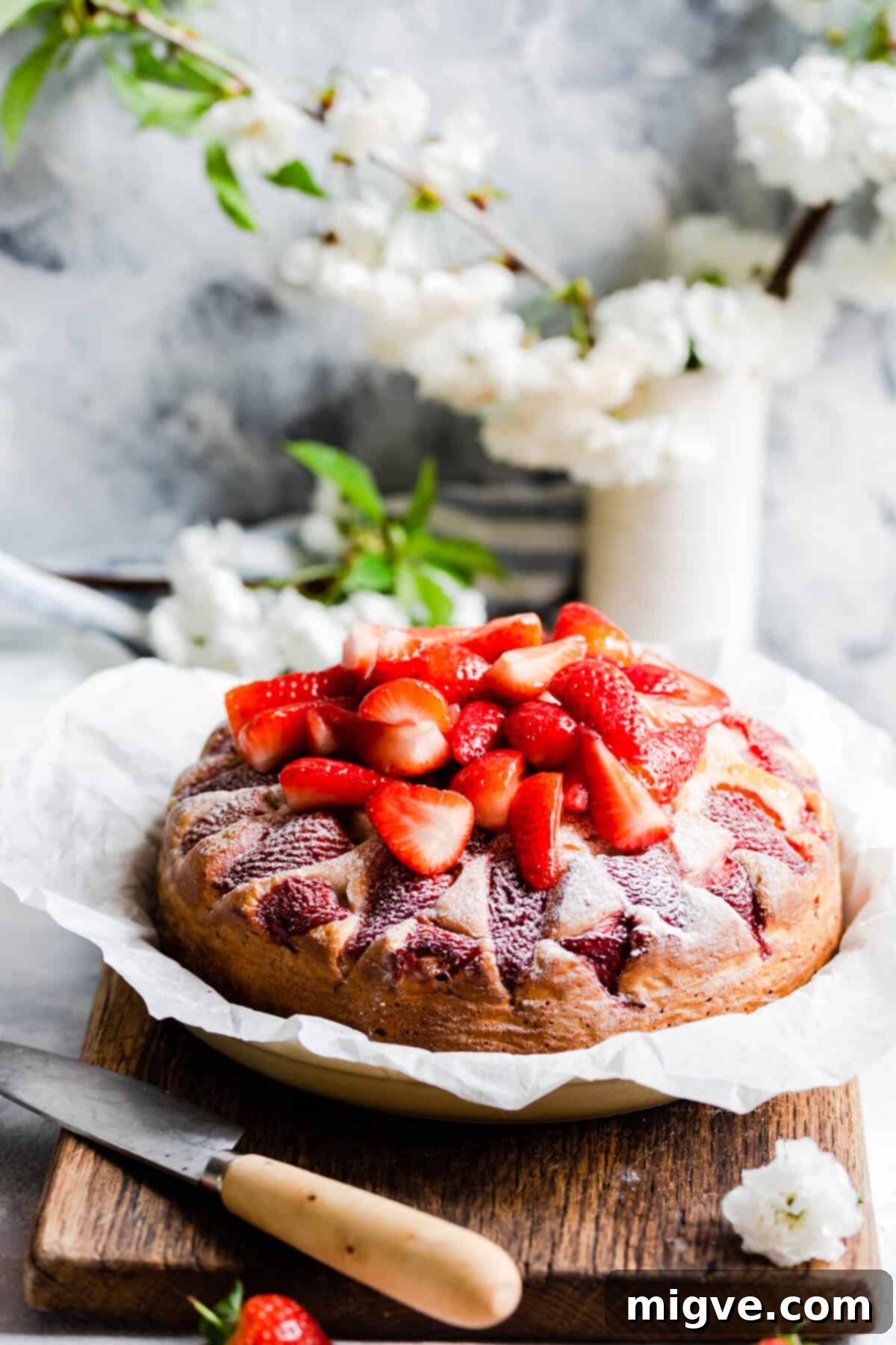 Straight-ahead shot of a simple, elegant fresh strawberry yogurt cake, generously topped with halved fresh strawberries.