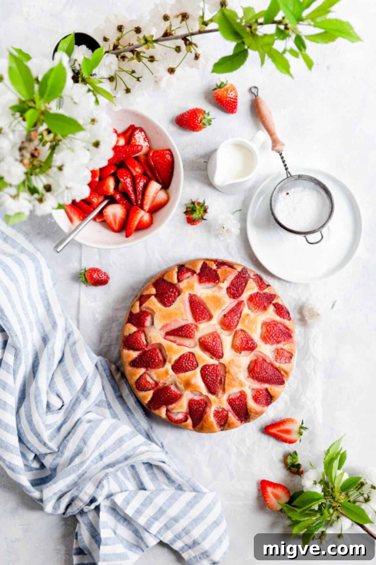 Top-down view of a freshly baked strawberry yogurt cake garnished with strawberries and a sprig of cherry blossom.