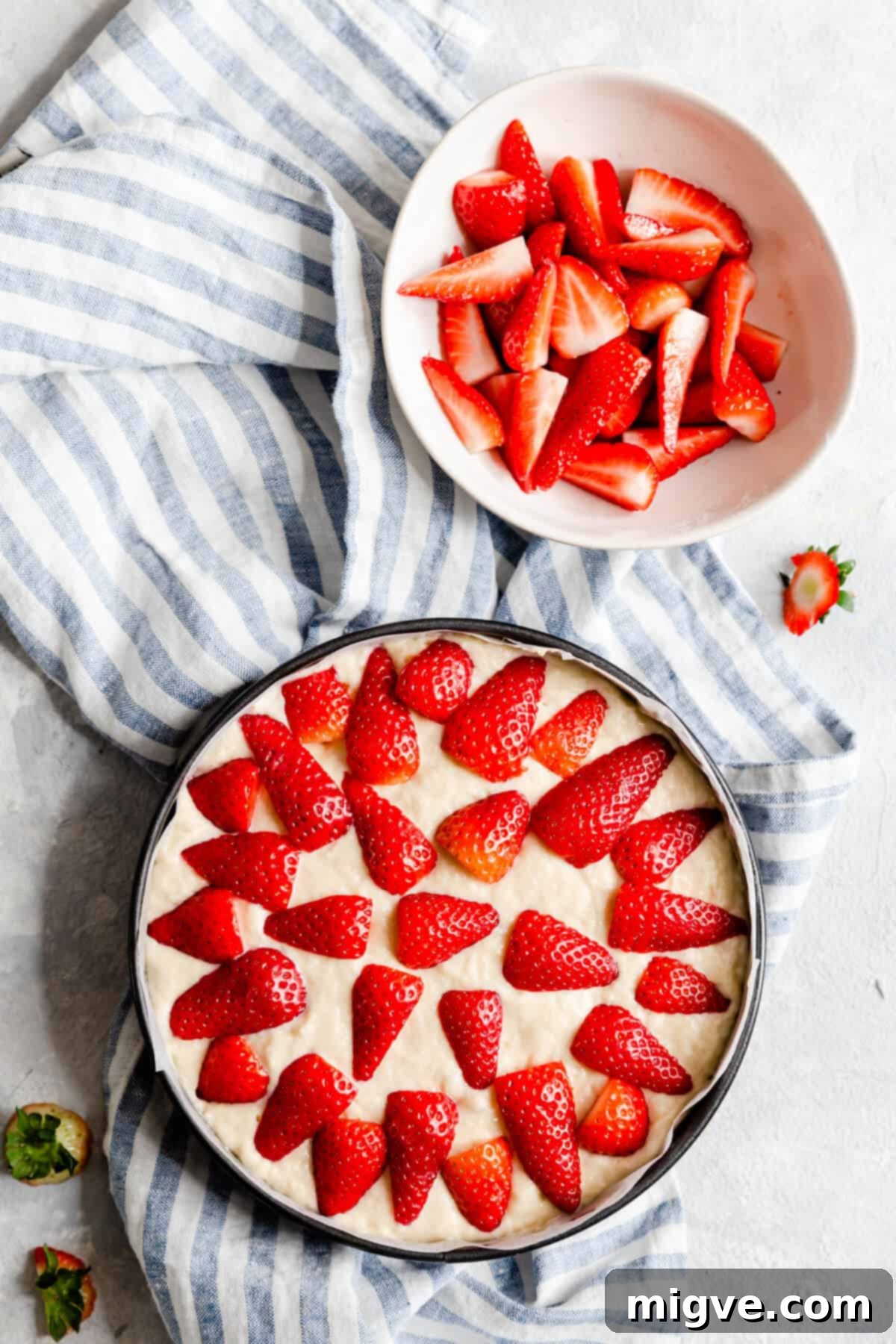 Top view of cake batter in a baking tin, already topped with a layer of fresh, halved strawberries, ready for baking.