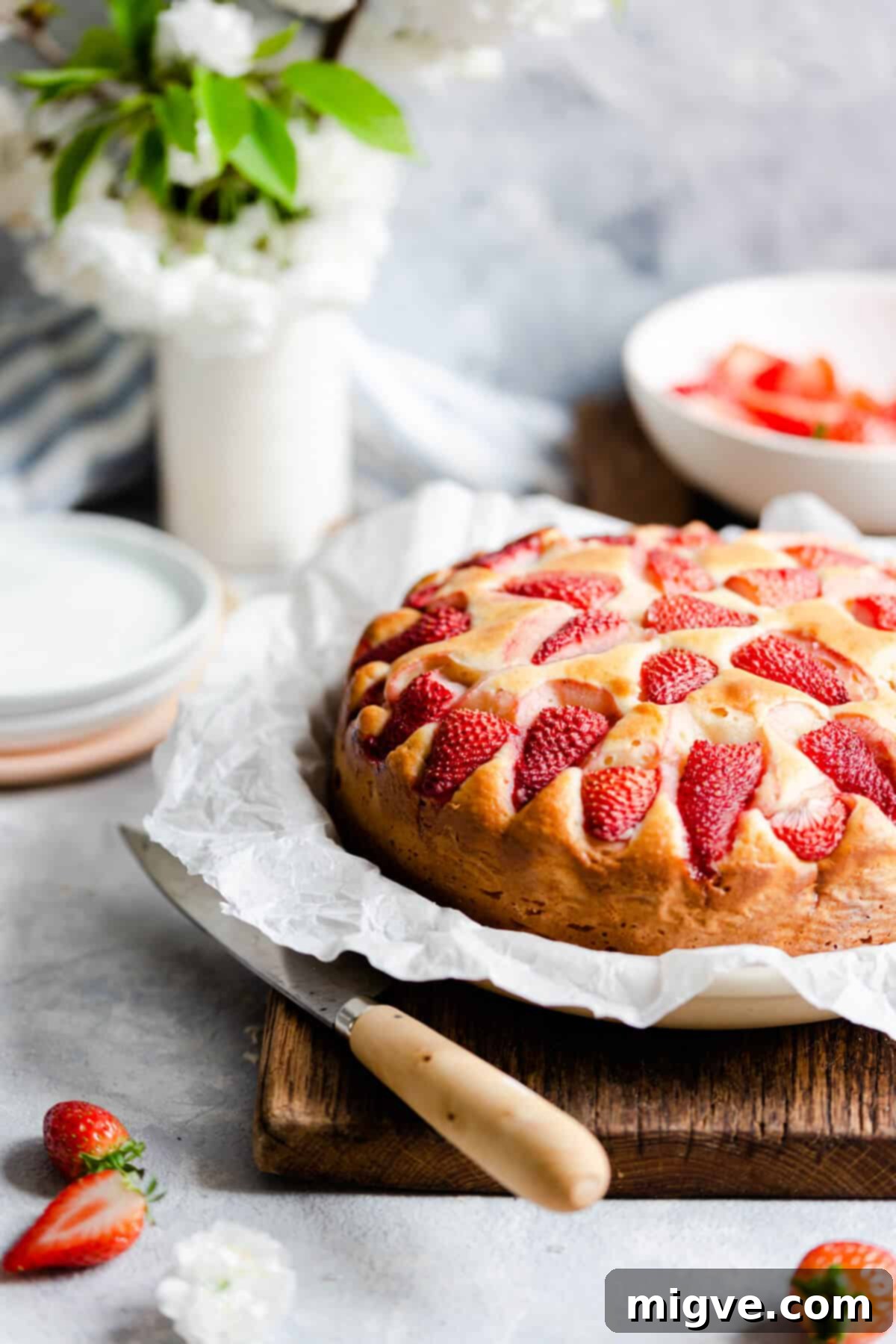 Side shot of the freshly baked strawberry yogurt cake on a wooden chopping board, showcasing its golden crust and height.