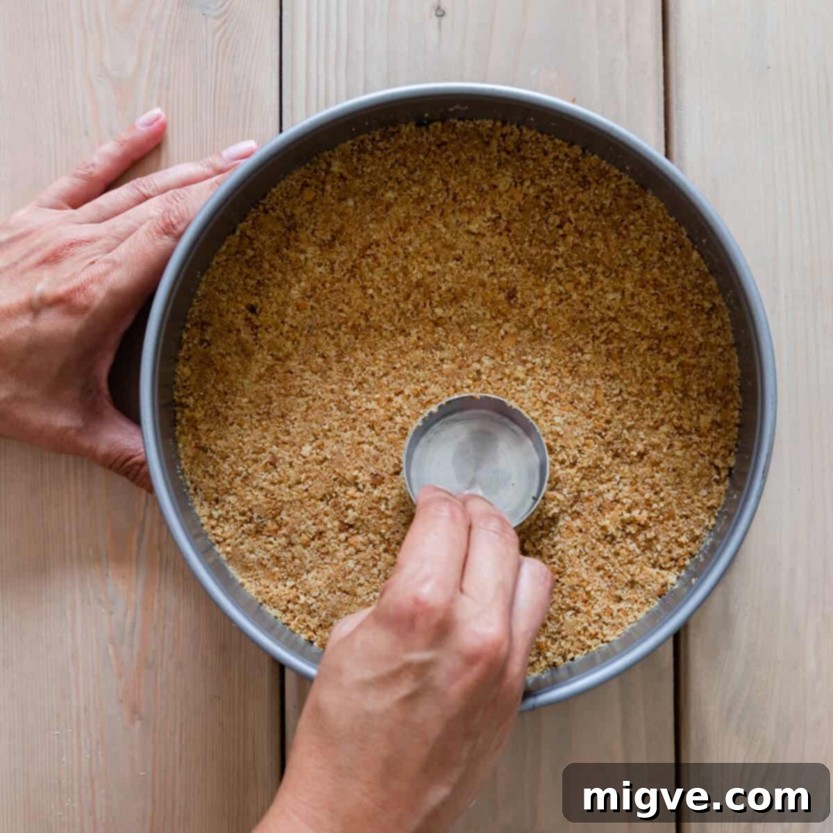 crushed biscuits being pressed into the base of round baking tin.