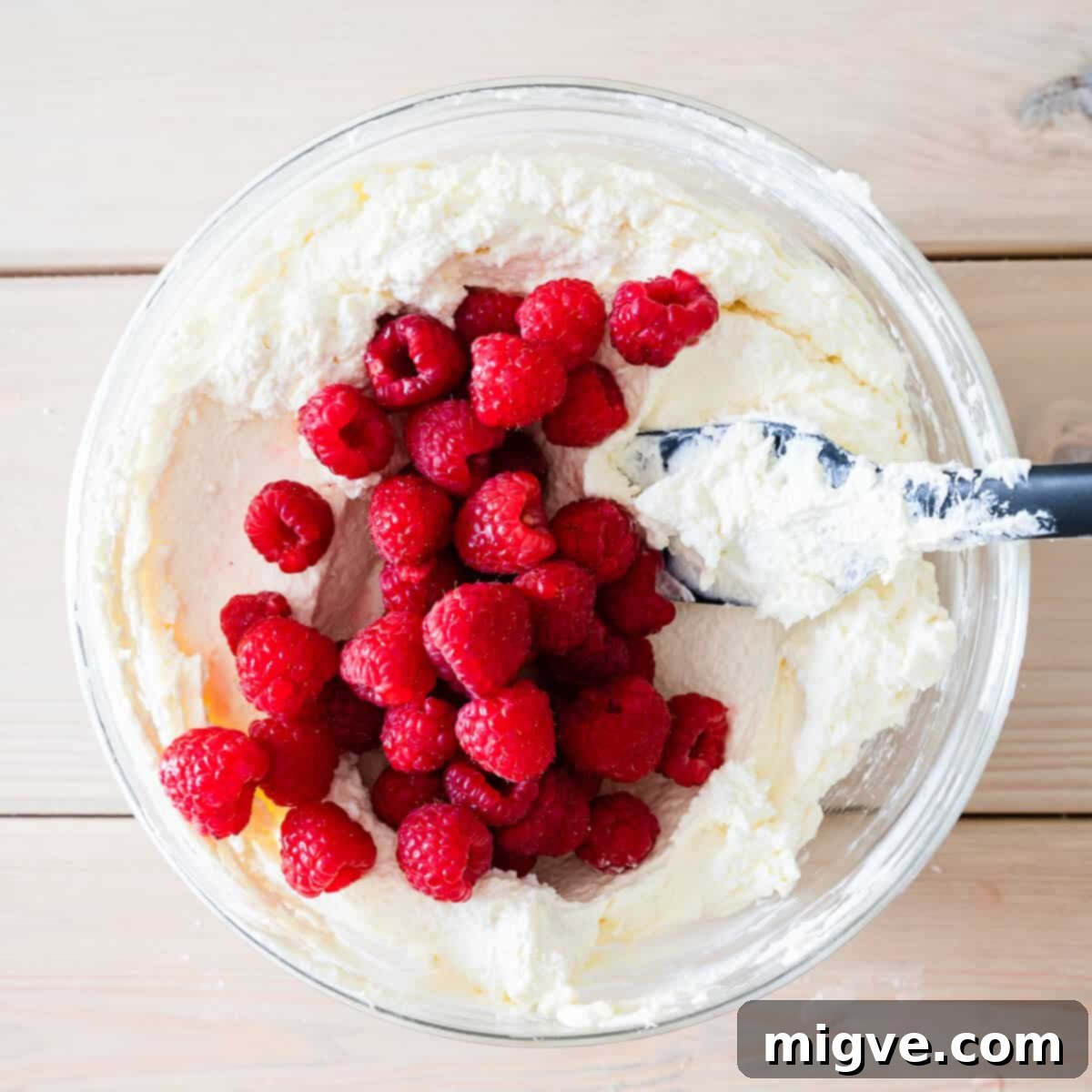 mixing bowl with cheesecake filling and fresh raspberries.