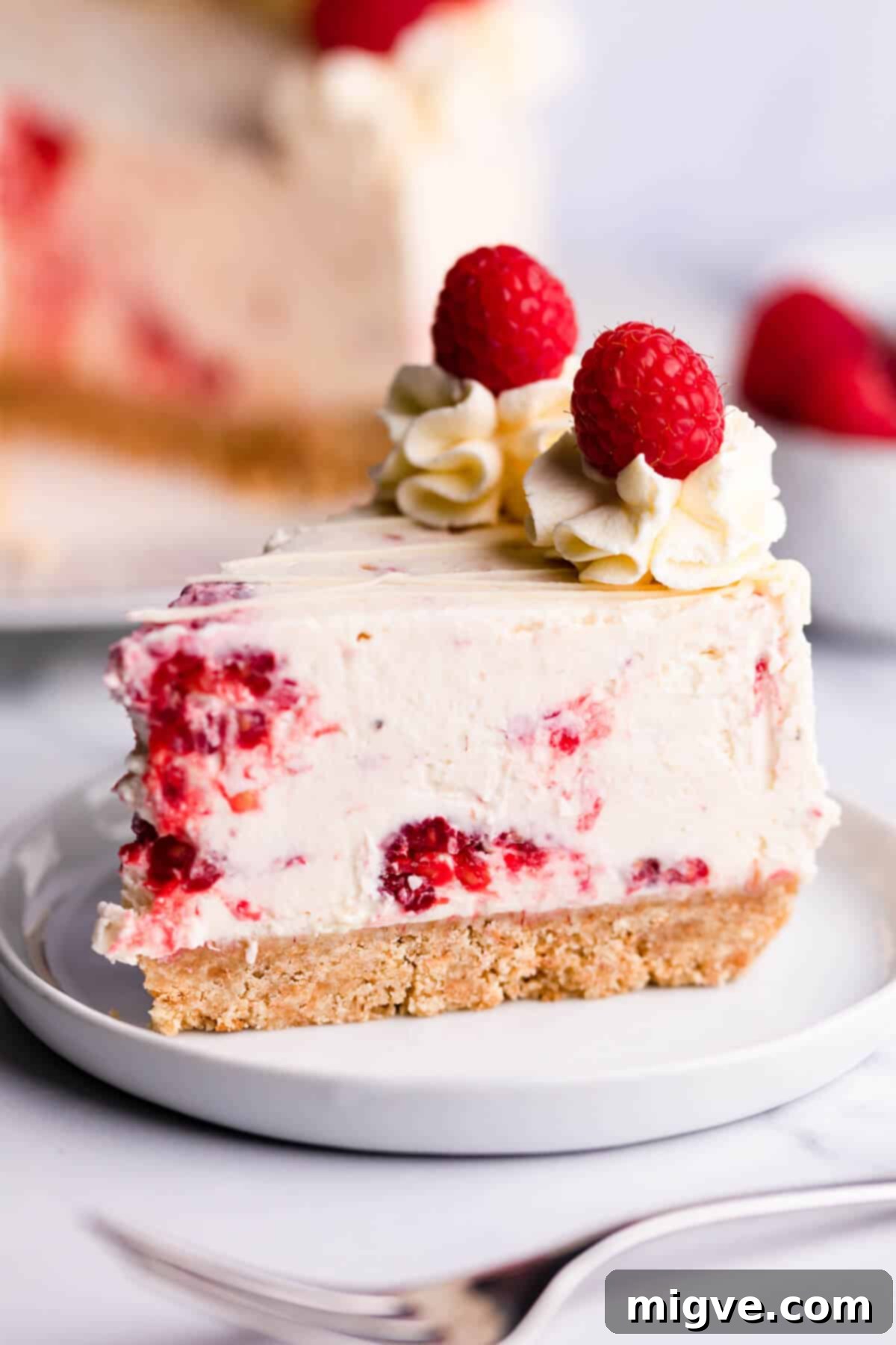 Slice of no bake cheesecake with fresh raspberries and white chocolate.