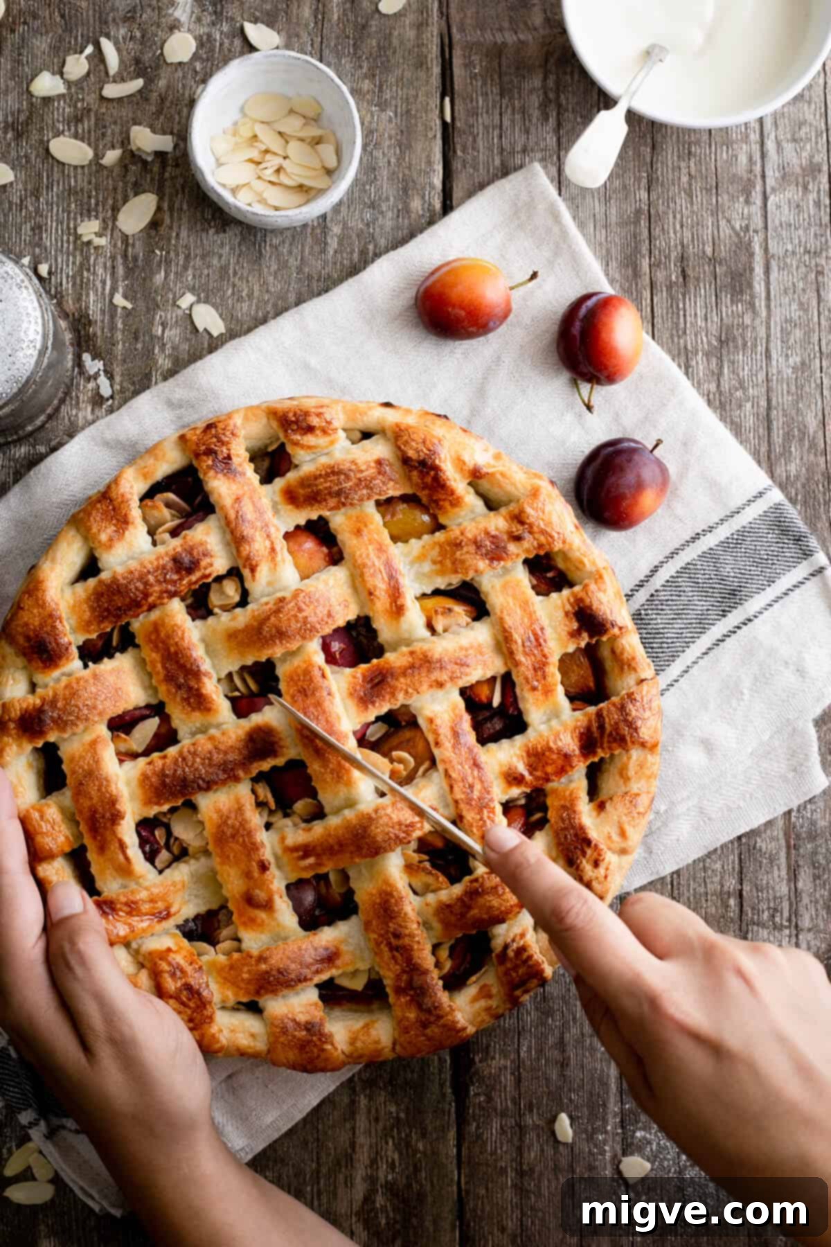 A freshly baked plum pie with a golden lattice crust, sliced to reveal the vibrant purple plum and almond filling beneath, perfect for a cozy afternoon treat.