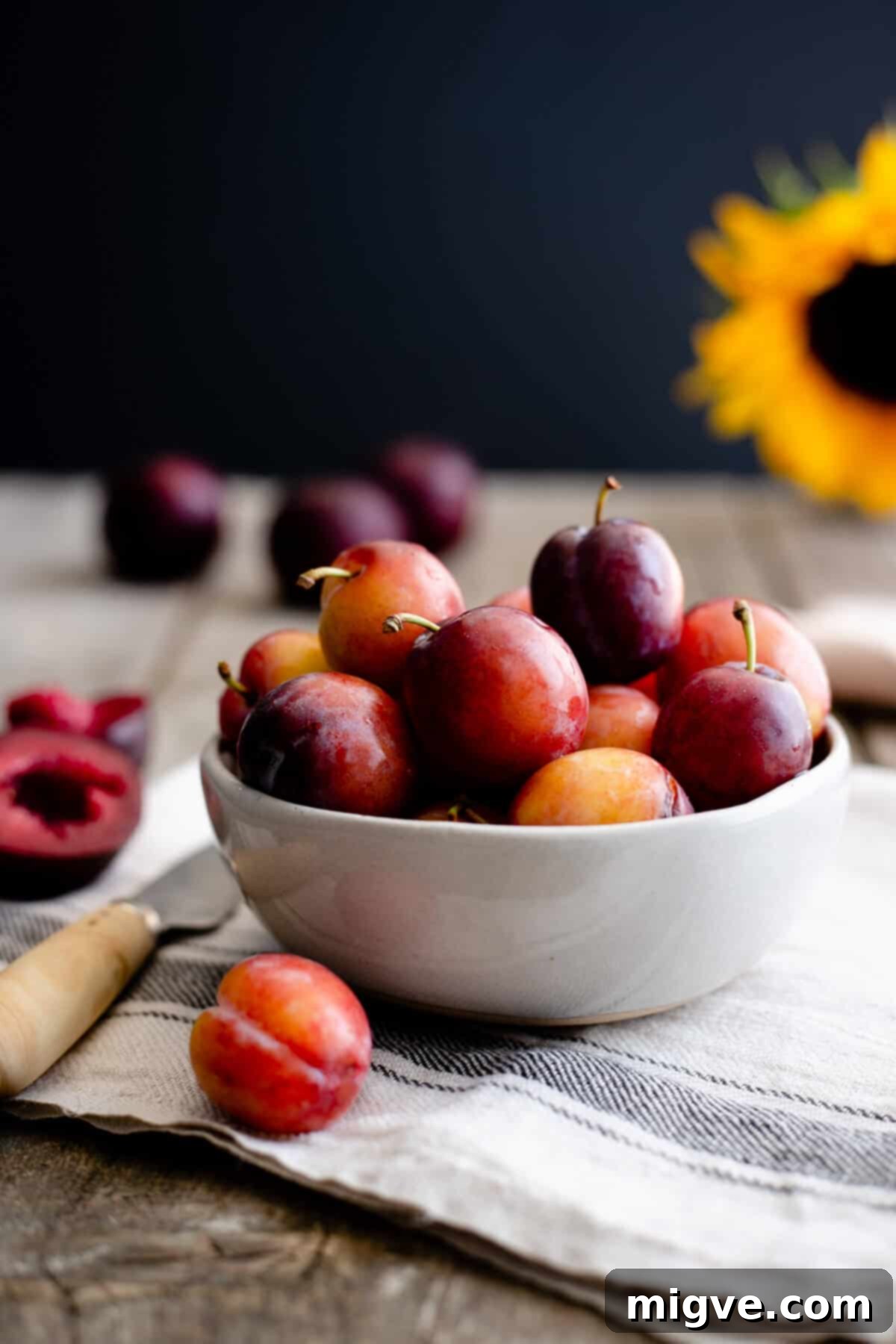 A small, rustic bowl overflowing with fresh, vibrant red and purple plums, ready to be transformed into a delicious pie.