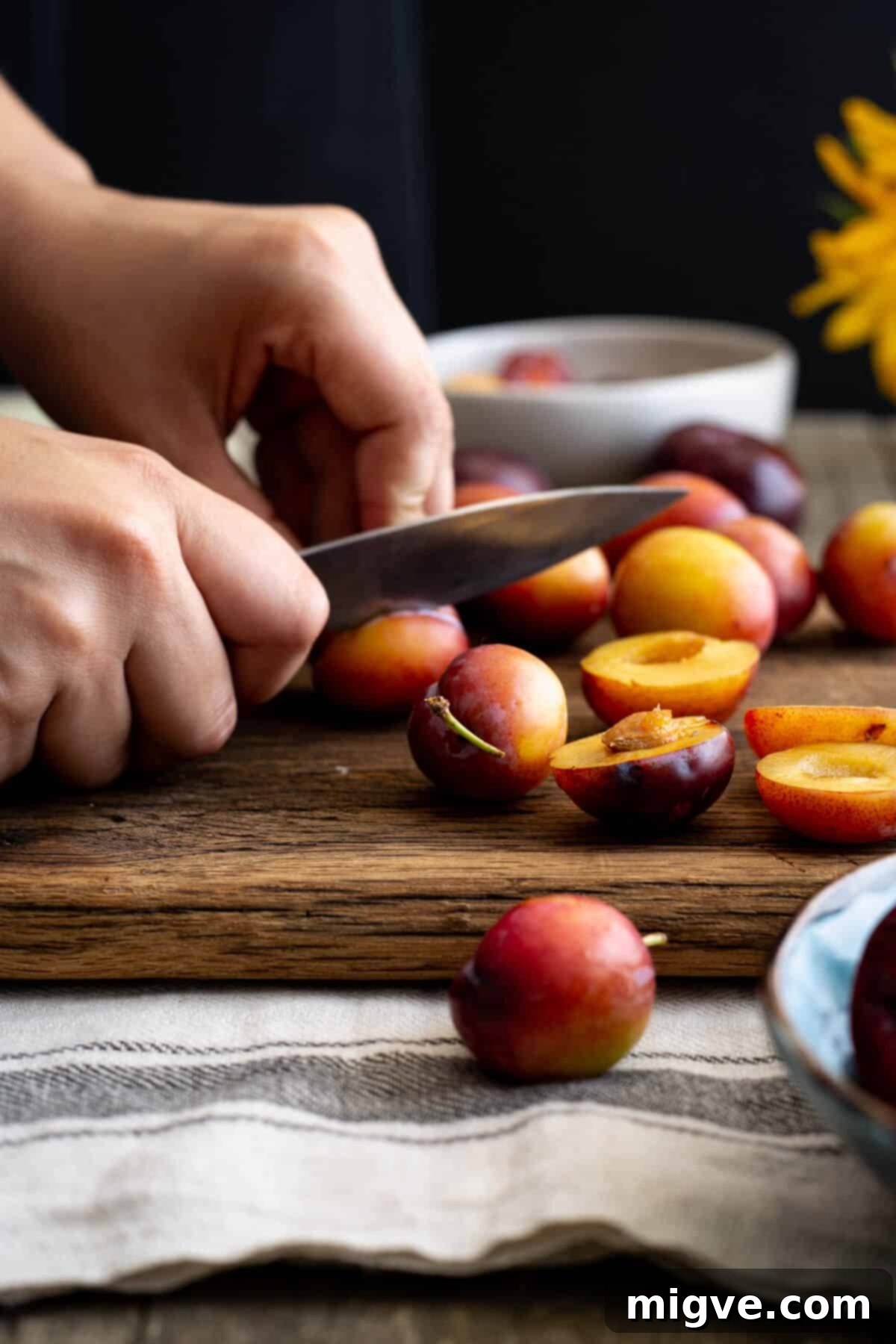 Close-up of fresh plums being halved and destoned on a wooden cutting board, preparing them for the pie filling.