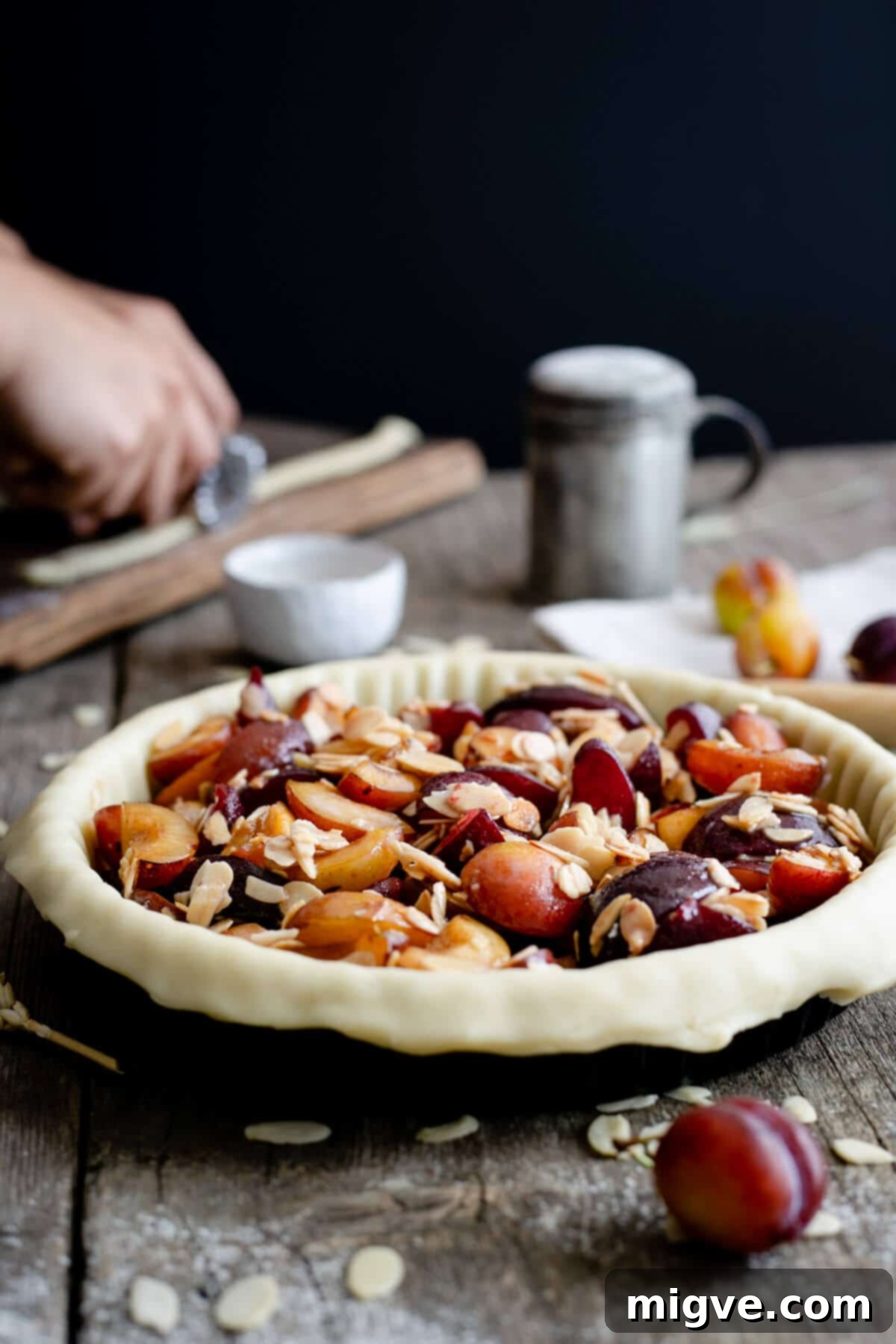 An unbaked plum pie with almonds, featuring a beautifully crafted lattice crust, patiently waiting to be placed in the oven.