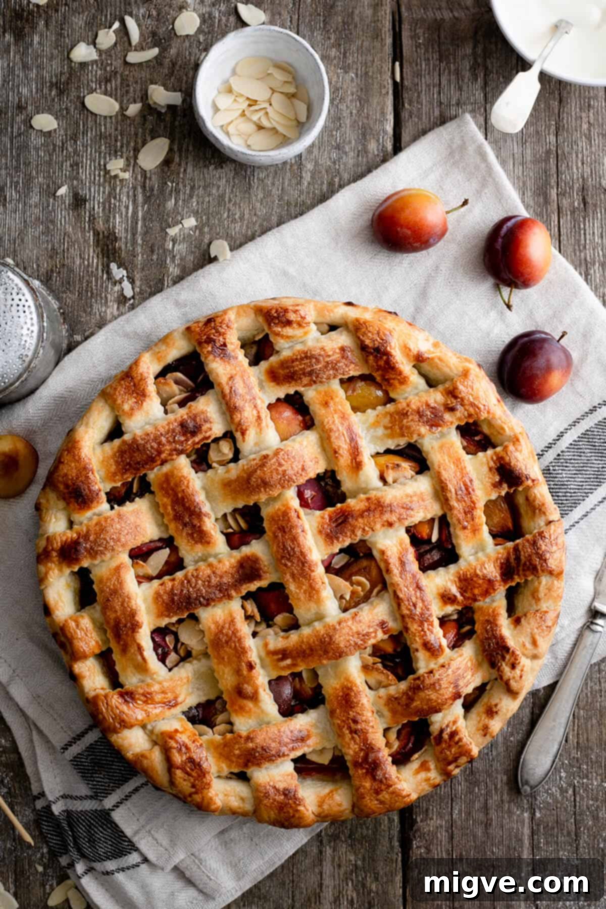 A close-up of a beautifully baked plum and almond pie, highlighting the perfectly executed decorative lattice pattern on its golden crust.