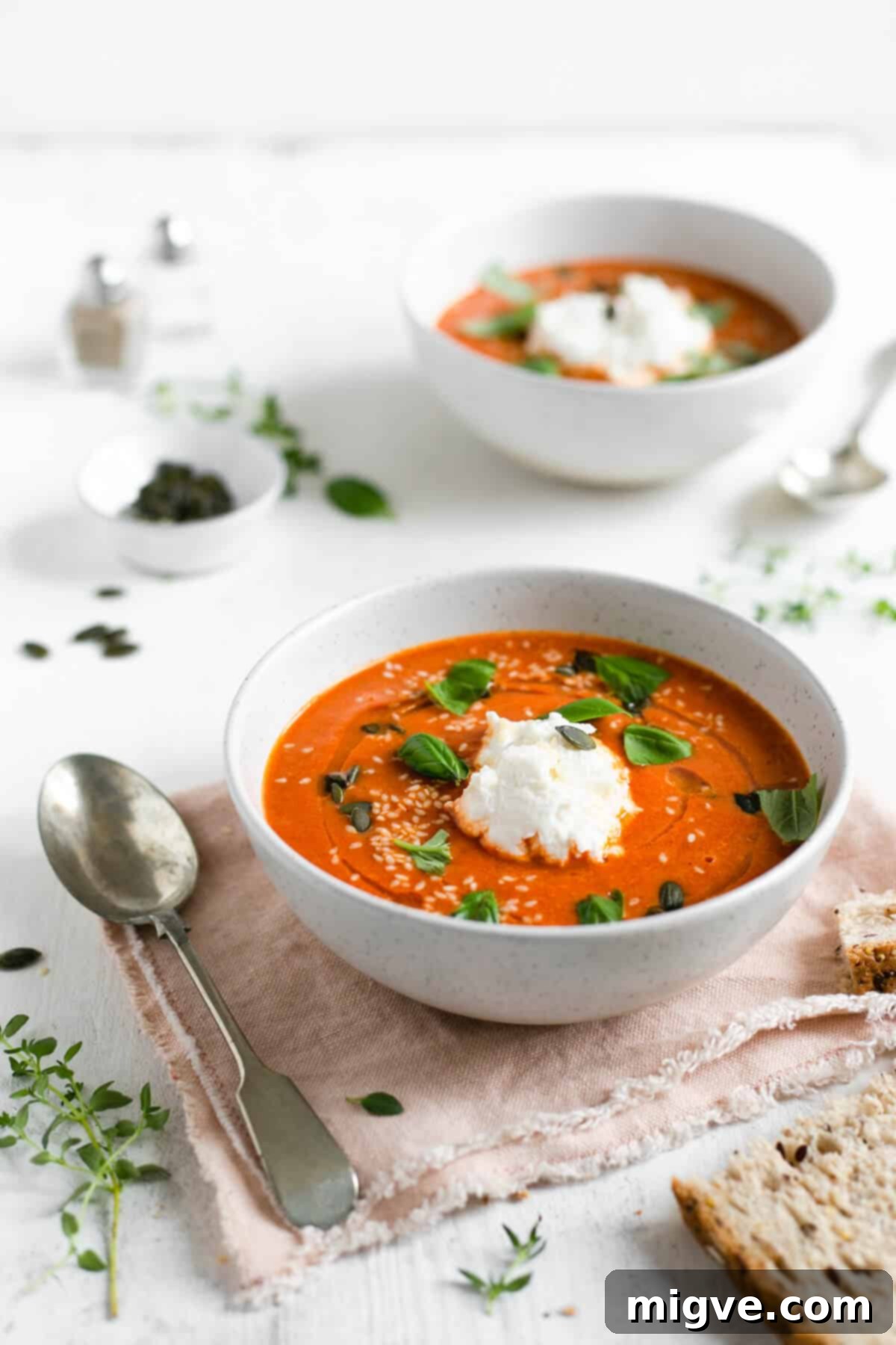 Two rustic bowls of roasted tomato and red pepper soup, garnished with sesame and pumpkin seeds