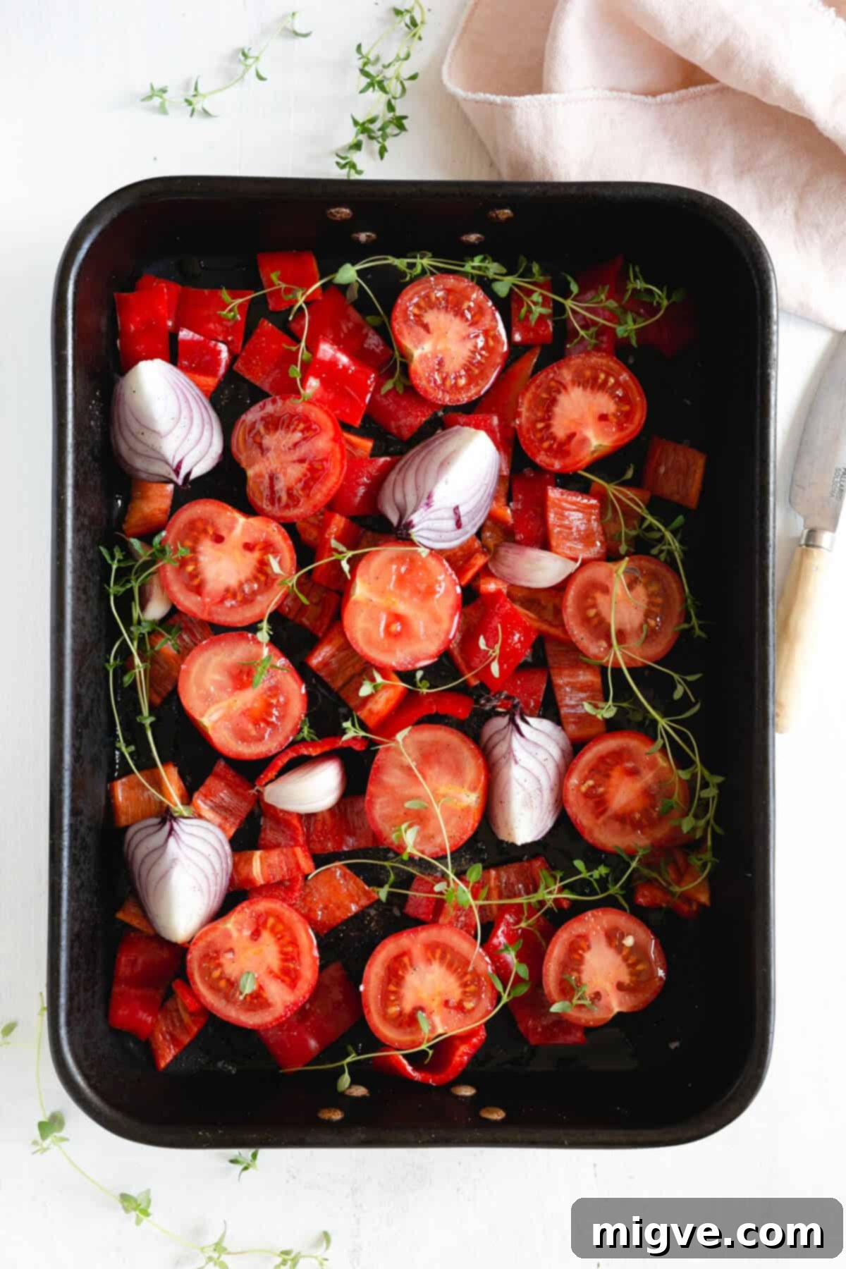 Freshly cut tomatoes and red romano peppers drizzled with olive oil in a roasting tin, ready for the oven