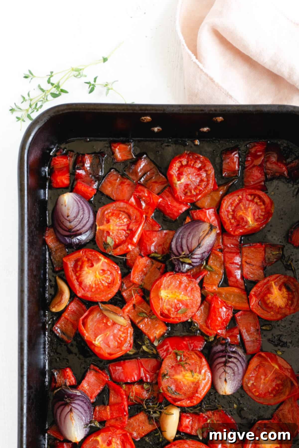 Roasted tomatoes, red romano peppers, and red onions with herbs in a roasting tin, after cooking