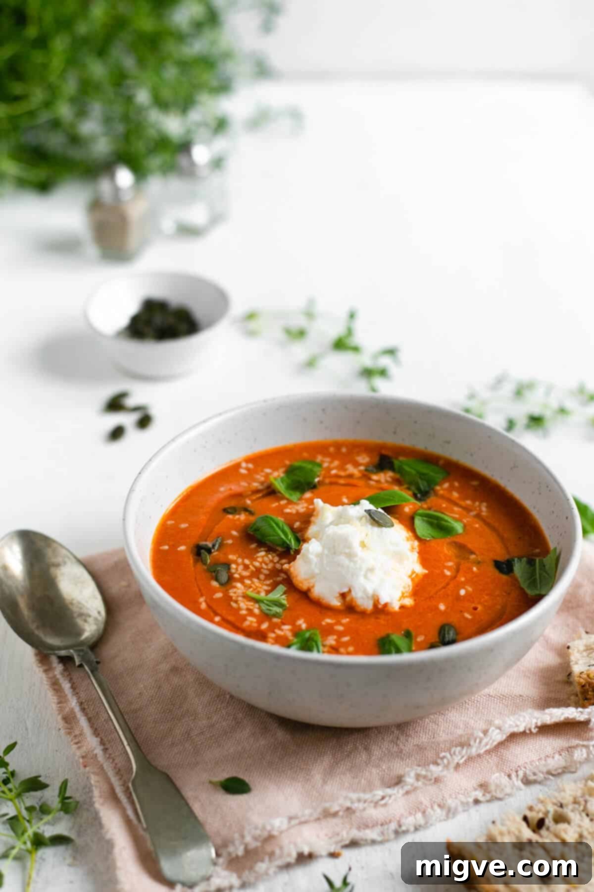 Small bowl of roasted tomato and red pepper soup topped with fresh basil leaves and ricotta cheese