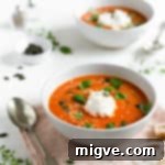 Two bowls of roasted tomato soup topped with sesame and pumpkin seeds