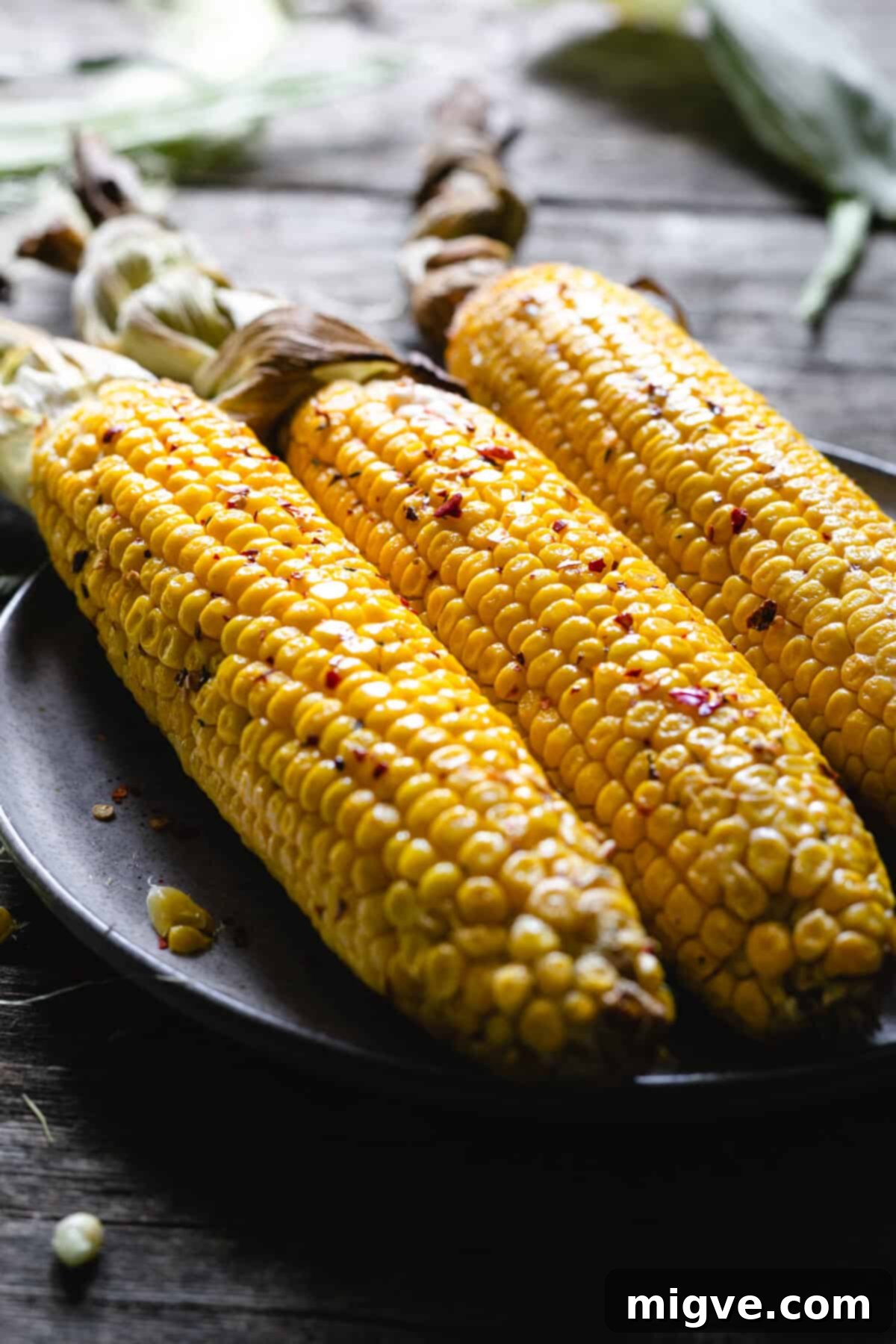 Three large corn cobs in chilli butter on a plate, ready to be served