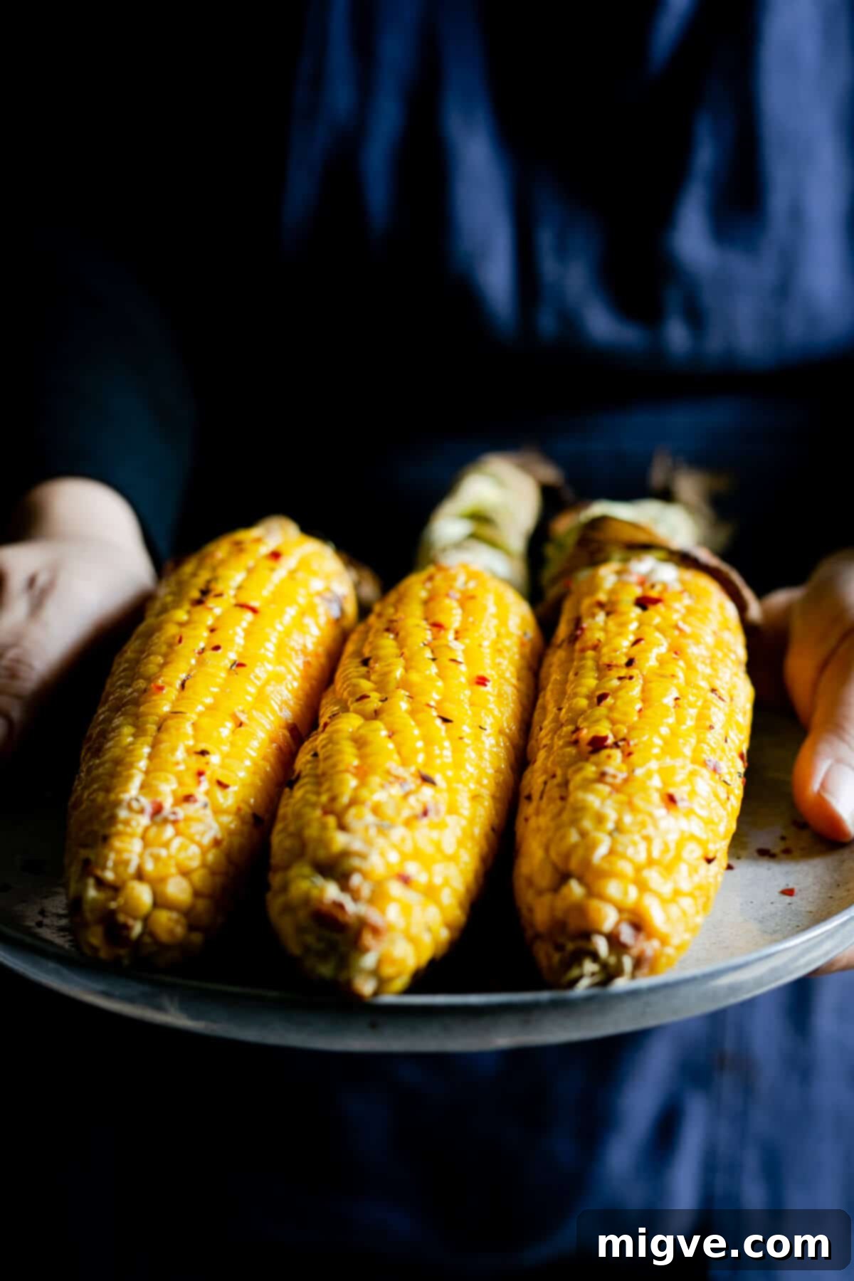 A person holding a plate with perfectly cooked corn cobs coated in vibrant chilli butter