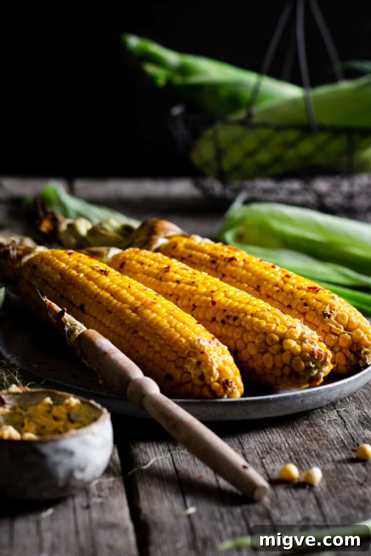 Three corn cobs on a plate, glistening with chilli butter, ready to be enjoyed