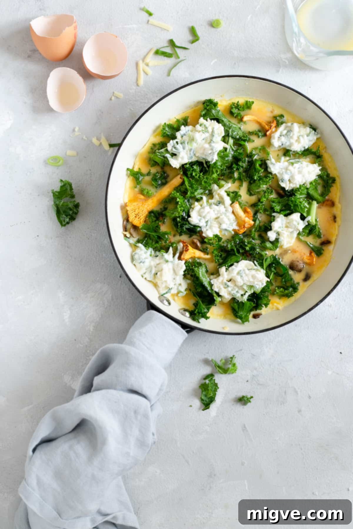 Mushroom and kale frittata baking in a frying pan, topped with melting cheese.