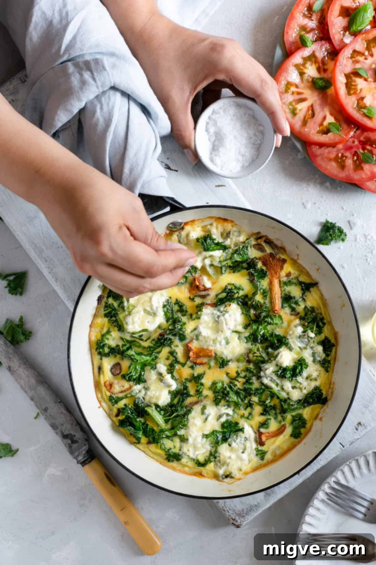 A hand adding salt to the mushroom and kale frittata in a frying pan.