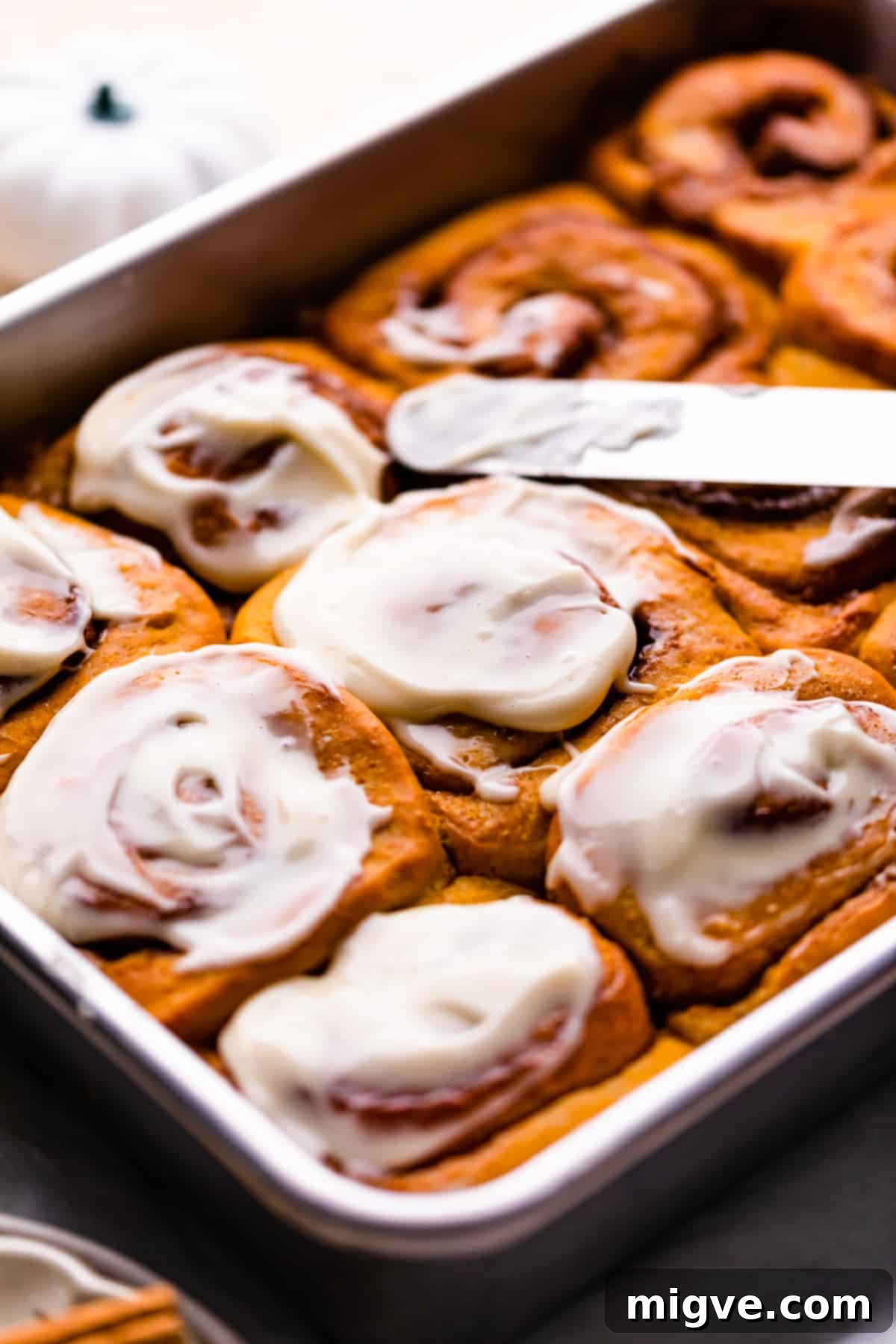 Fresh pumpkin rolls with cinnamon, generously topped with cream cheese icing, ready to be served.