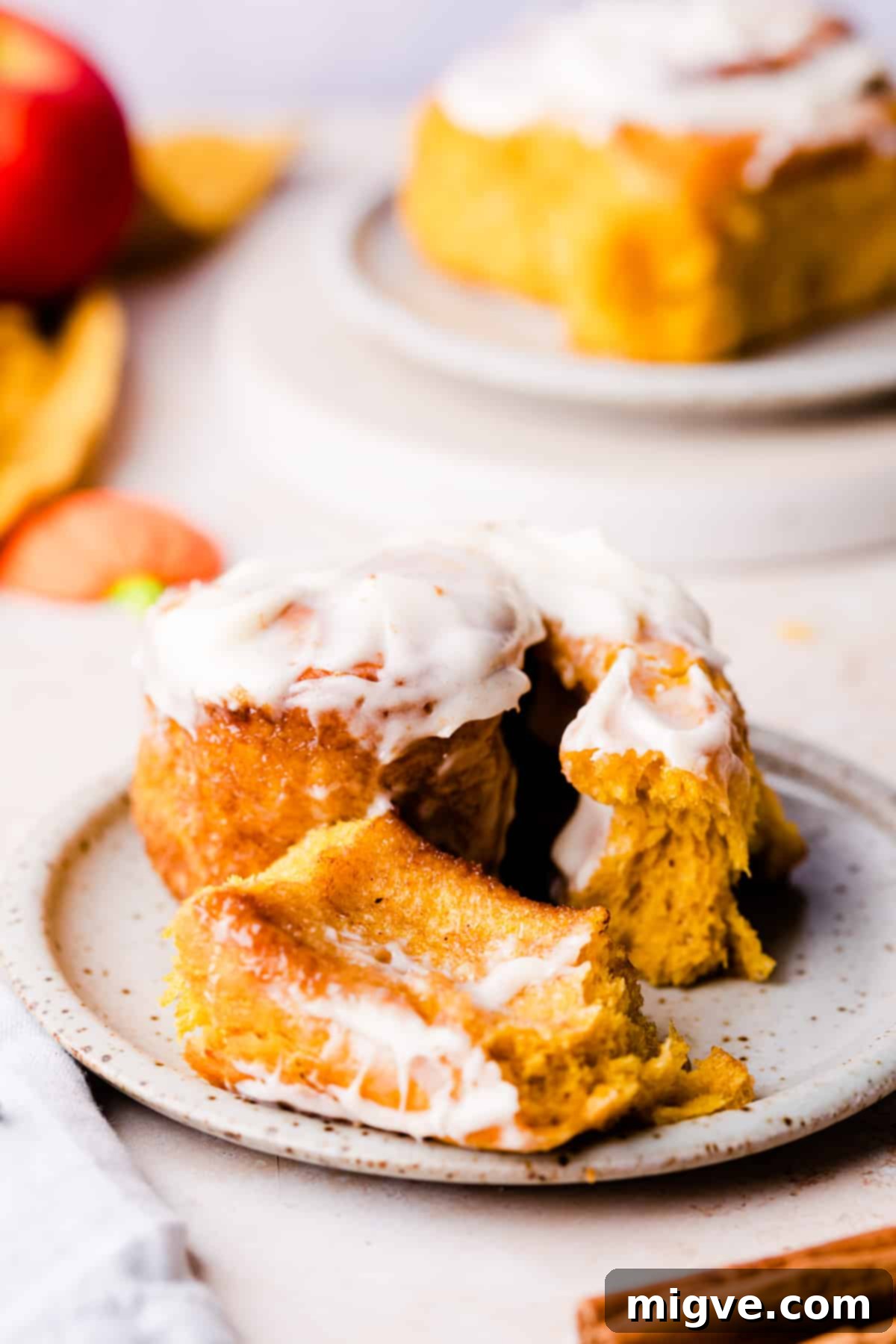 A single pumpkin cinnamon bun with a piece gently taken out of it, showcasing the soft interior, on a small plate.