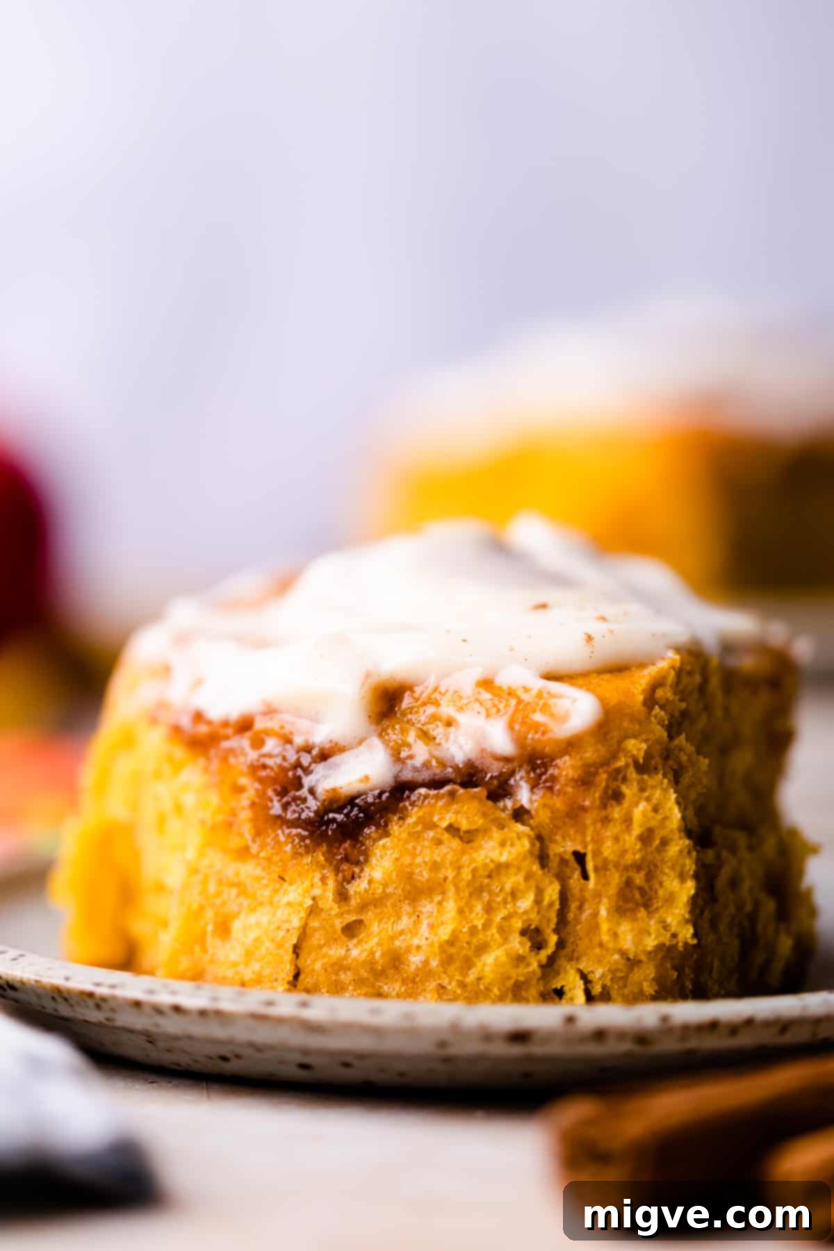 A homemade pumpkin roll with cinnamon and a generous dollop of cream cheese glaze on top, presented on a small plate.