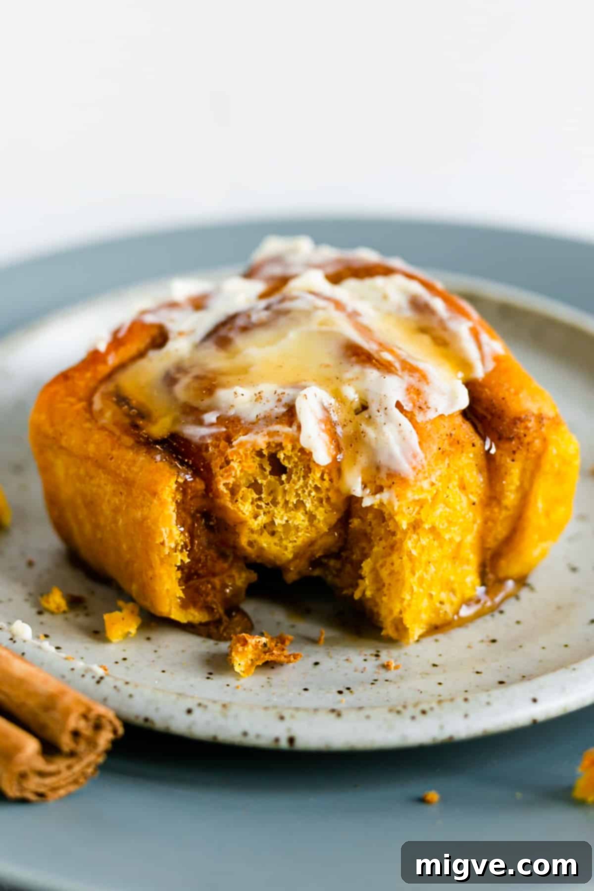 An individual pumpkin roll with ample icing on top and a delightful bite taken out, resting on a small plate.