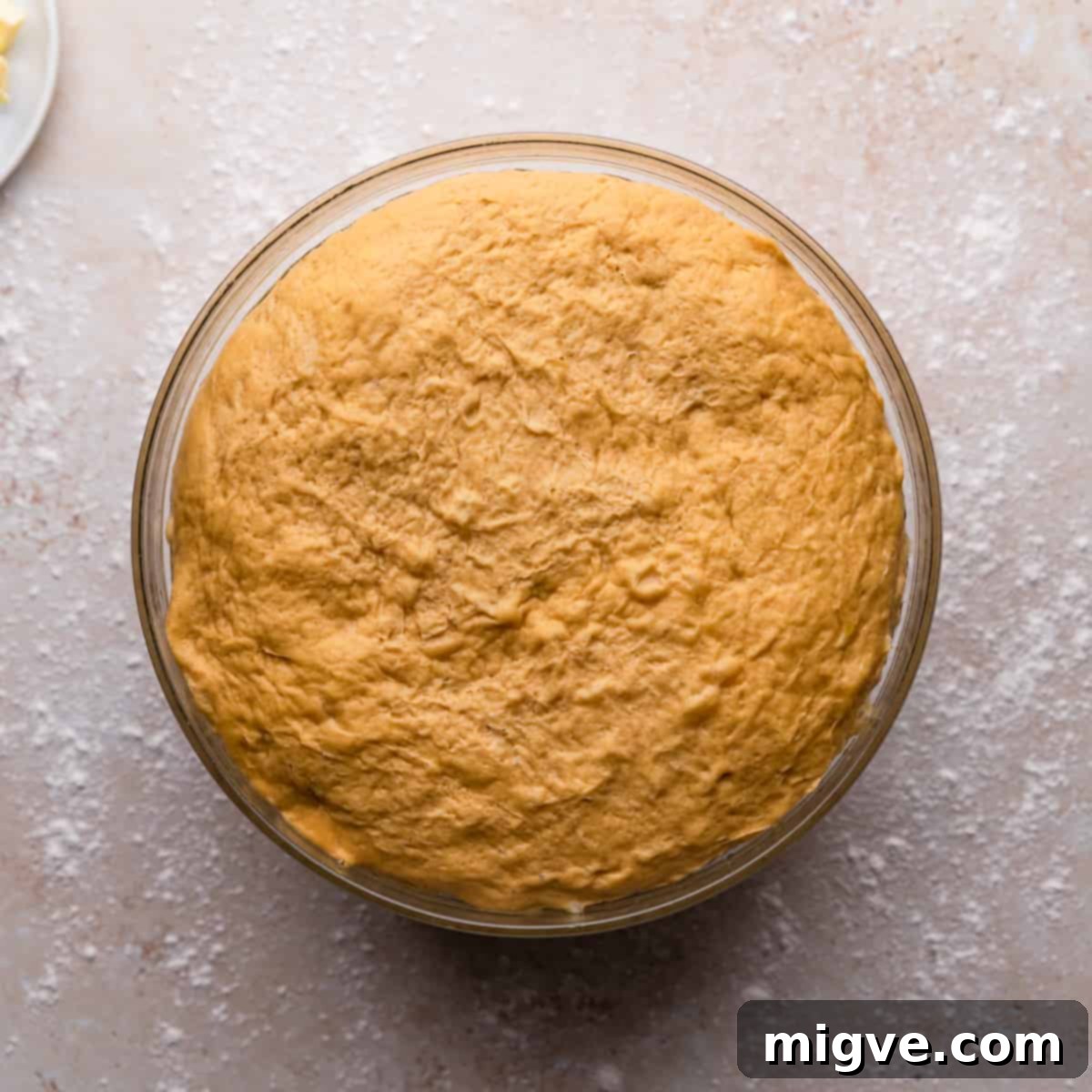 Glass bowl with risen dough for pumpkin rolls with cinnamon, showing it has doubled in size.