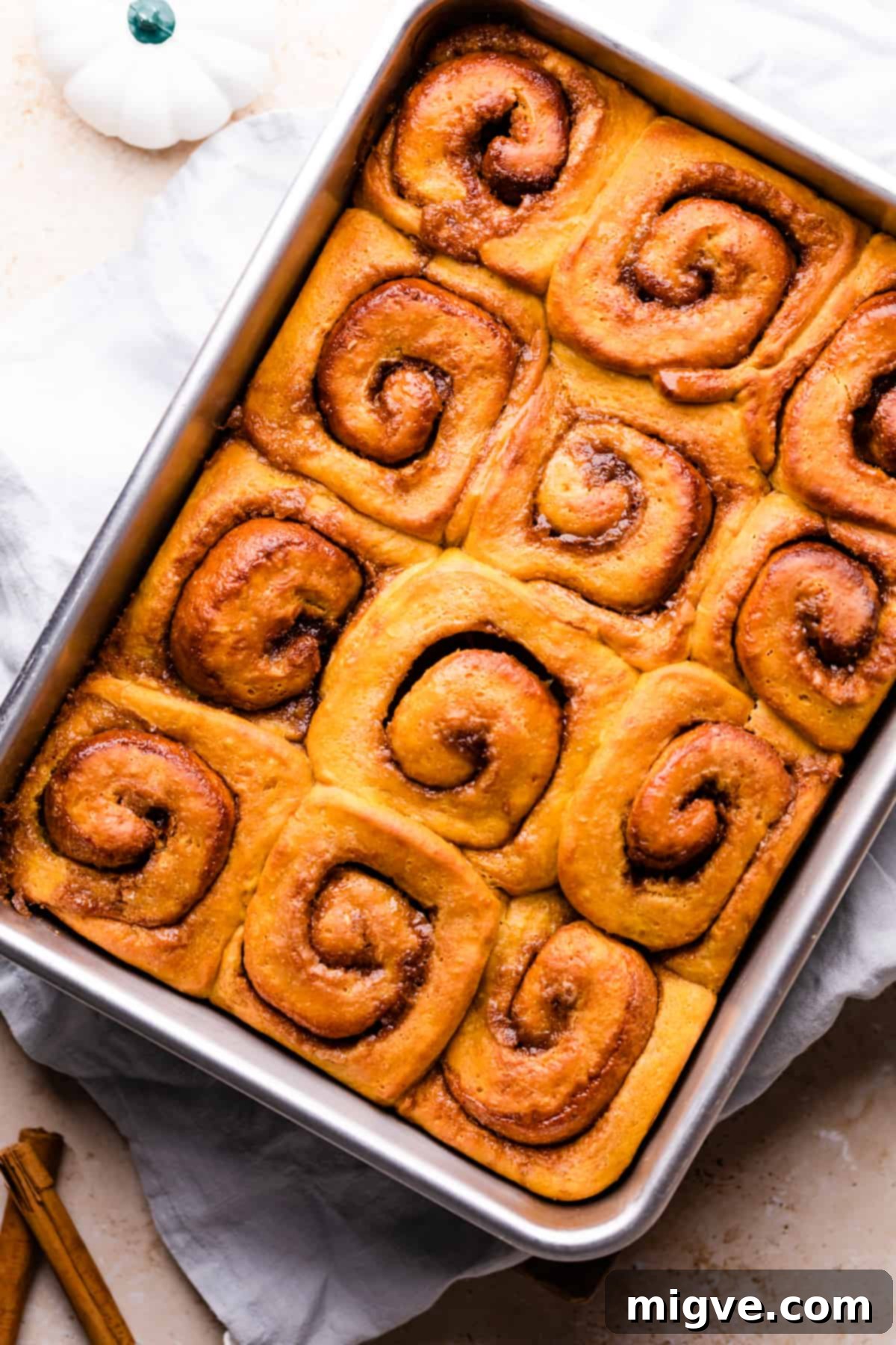 Baked pumpkin rolls with a visible cinnamon swirl in a rectangular baking dish, fresh from the oven.