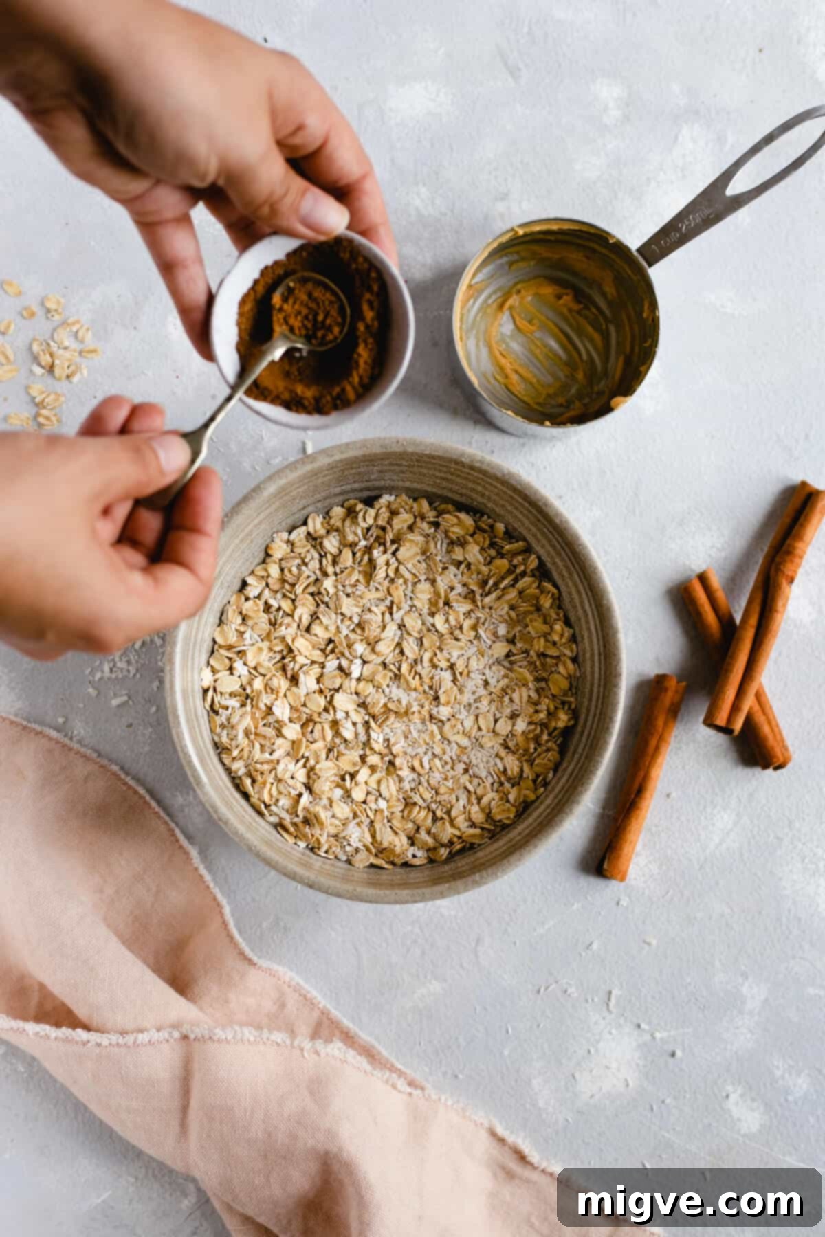 Spiced Coconut Peanut Power Bites 3 Overhead shot of a bowl with oats and shredded coconut with someone adding aromatic mixed spice to the mixture for spiced energy bites