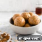 Spiced Coconut Peanut Power Bites 9 A straight-on angle shot of small bowl filled with coconut and peanut butter spiced energy bites with small jar of maple syrup in the background