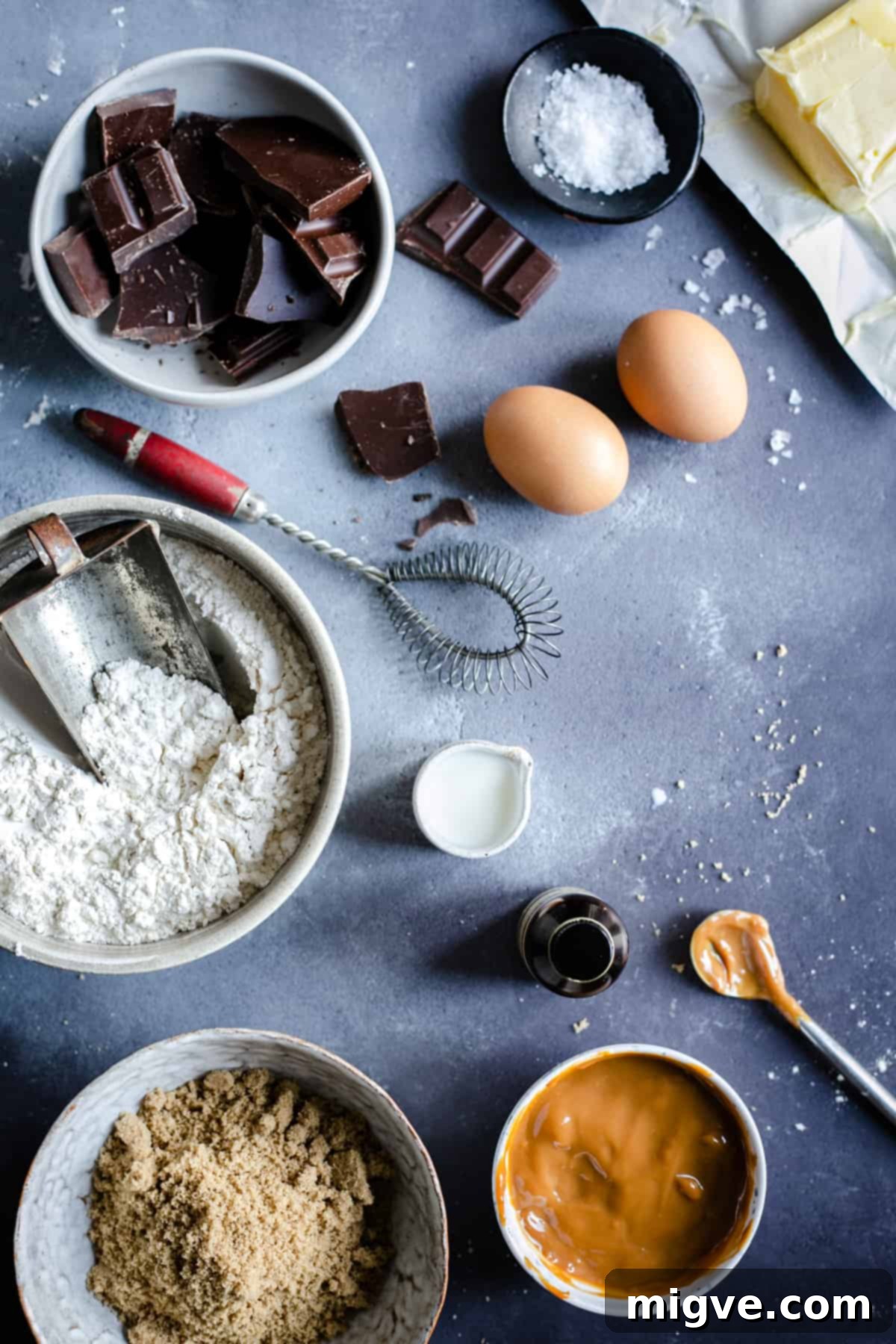 Decadent Chocolate and Salted Caramel Treats 3 An overhead shot showcasing the key ingredients for chocolate salted caramel cookies meticulously laid out on a rustic wooden surface, including chocolate chunks, flour, sugars, and eggs.