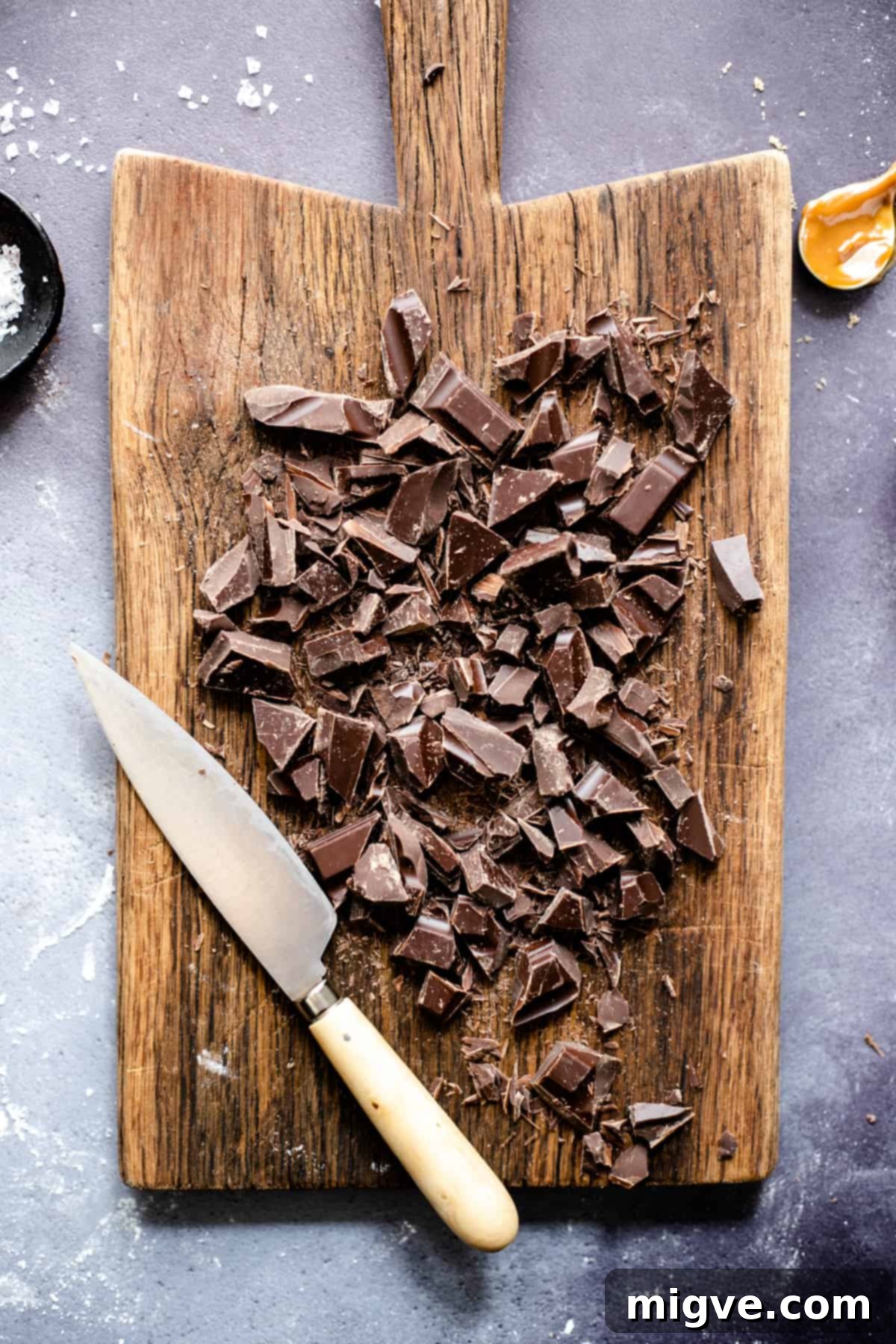 Decadent Chocolate and Salted Caramel Treats 4 An overhead shot of a wooden chopping board featuring dark chocolate chunks, ready to be incorporated into the cookie dough, emphasizing the quality ingredients.