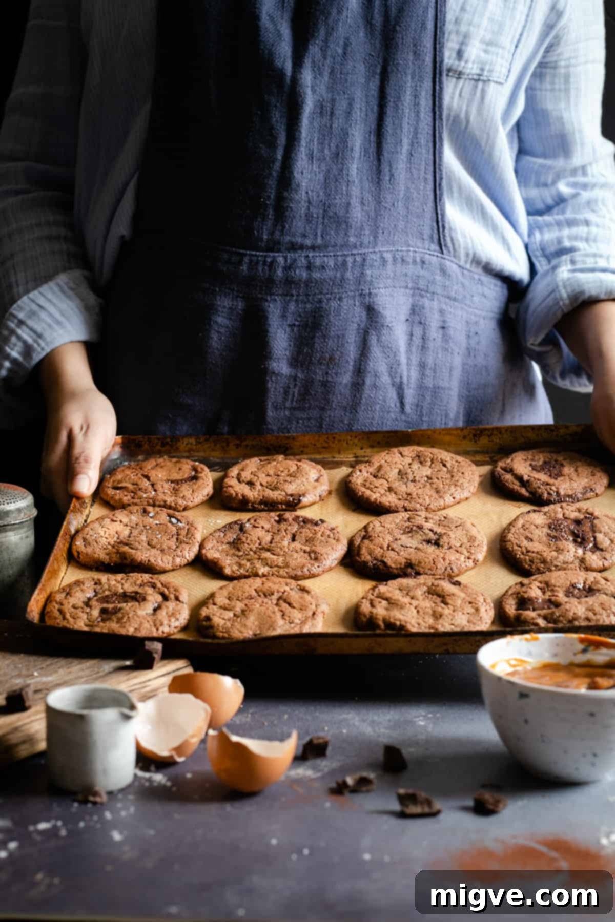 Decadent Chocolate and Salted Caramel Treats 6 A person proudly holding a baking tray overflowing with perfectly baked, golden-brown chocolate cookies, fresh from the oven and ready for the next step.