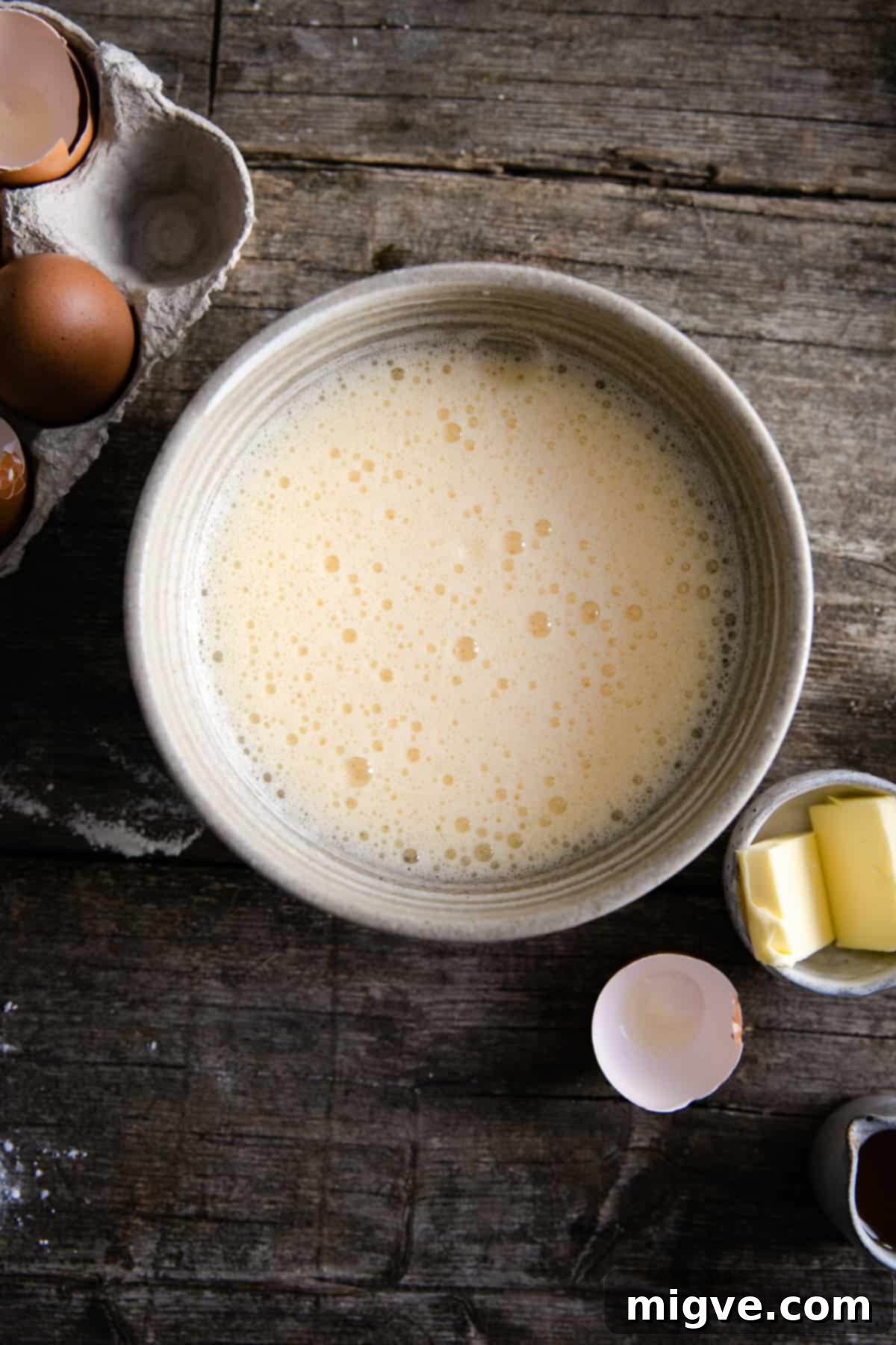 Berry Burst Dutch Delight 4 A bowl of light and frothy mixture of eggs and sugar, with some eggs and butter on the side, ready for Dutch baby batter