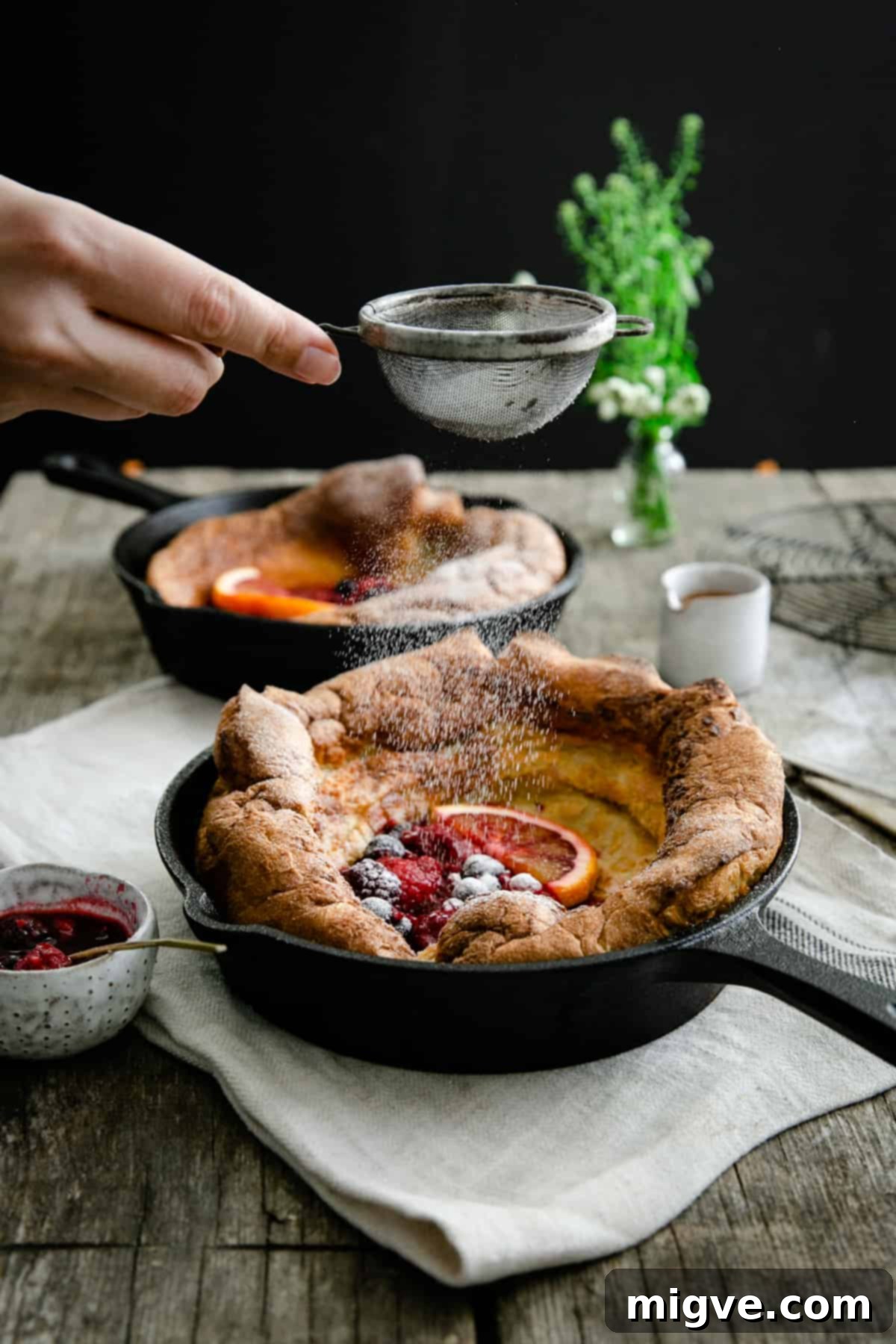Berry Burst Dutch Delight 6 Icing sugar being sprinkled on a mixed berry Dutch baby pancake with fresh berries