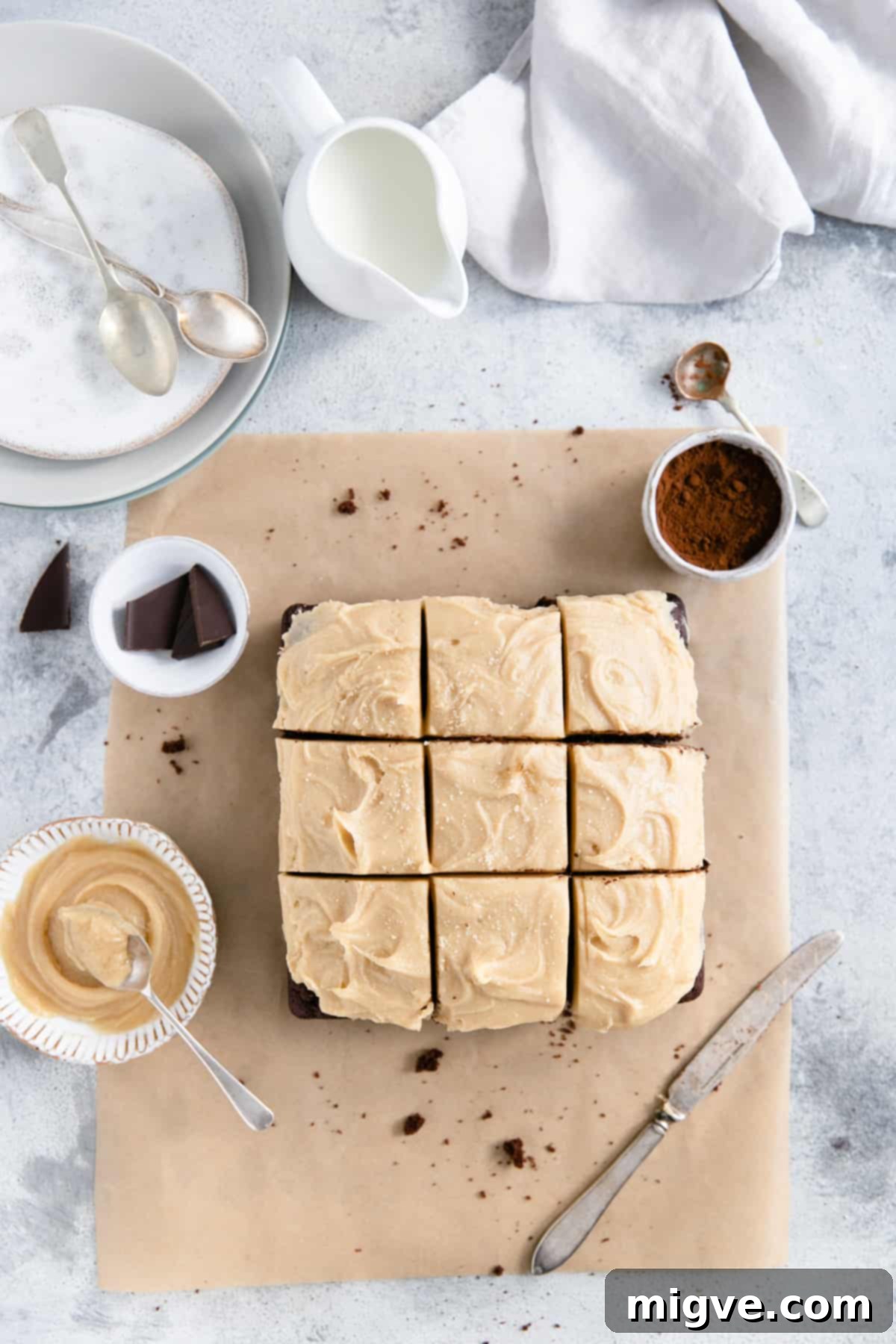 Overhead shot of chocolate brownies with peanut butter frosting on a white surface with some cocoa powder and peanut butter on site
