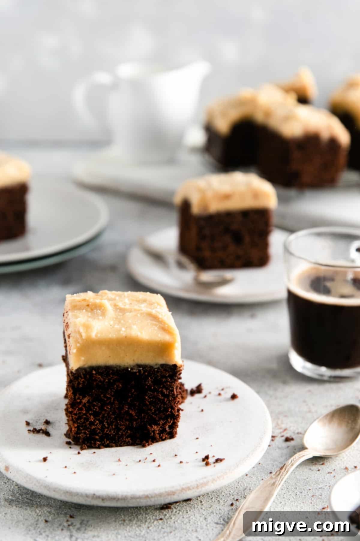 Straight ahead shot of chocolate brownie with peanut butter frosting on a small white plate with more brownies in the background