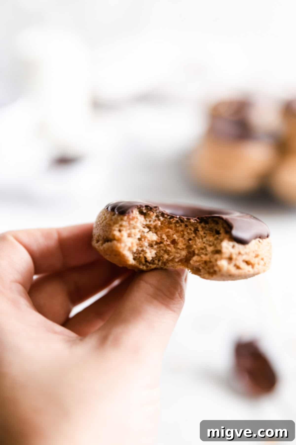 close up of a hand holding a baked doughnut with a small bite taken out of it