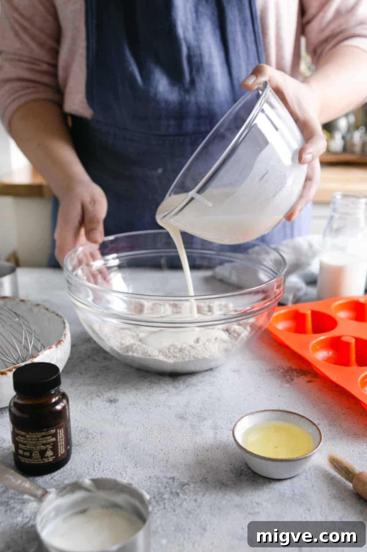 a person pouring the wet ingredients into a large bowl with dry ingredients for baked doughnuts