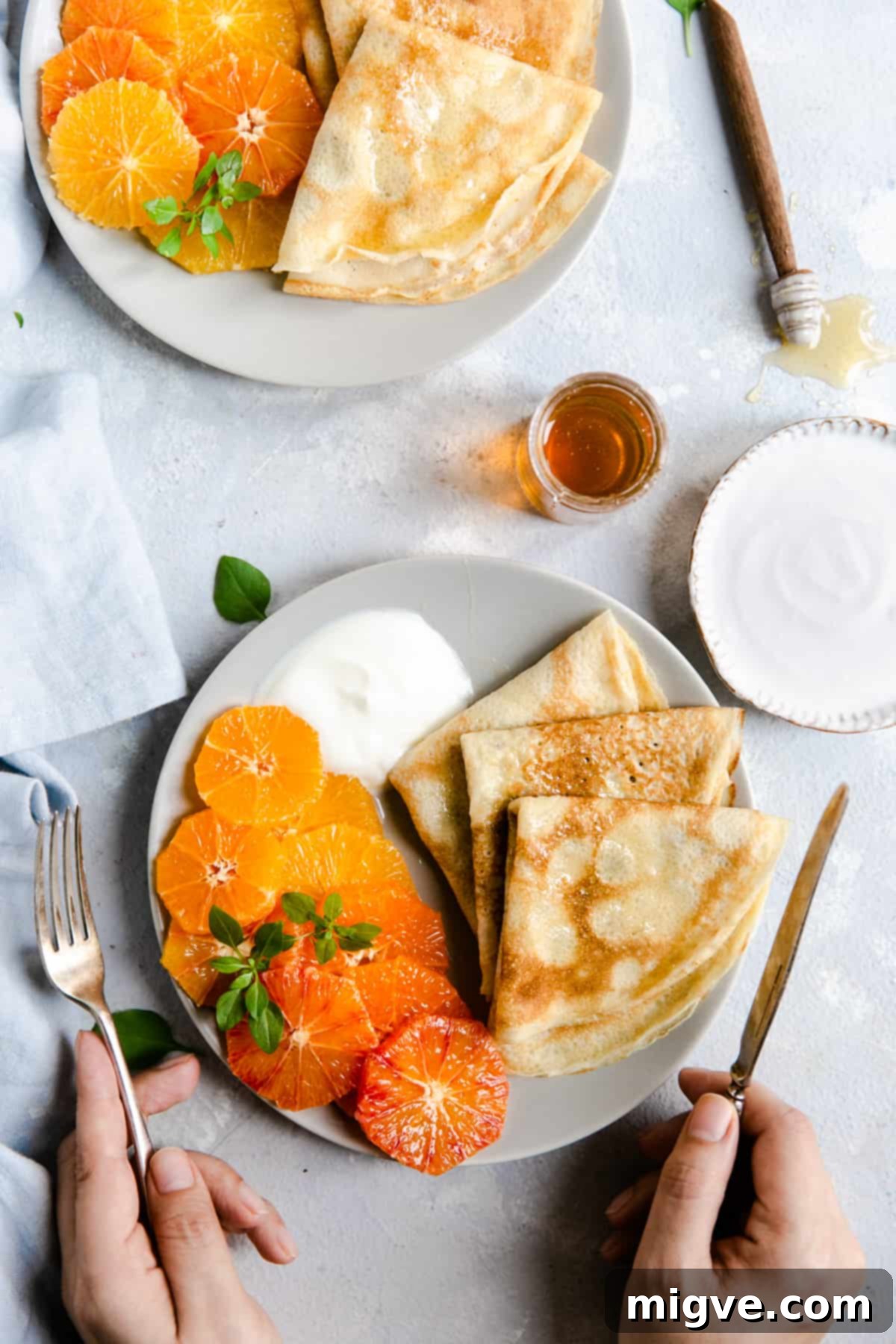Overhead shot of a plate with golden-brown crepes, vibrant citrus slices, and a dollop of creamy yogurt with a honey drizzle