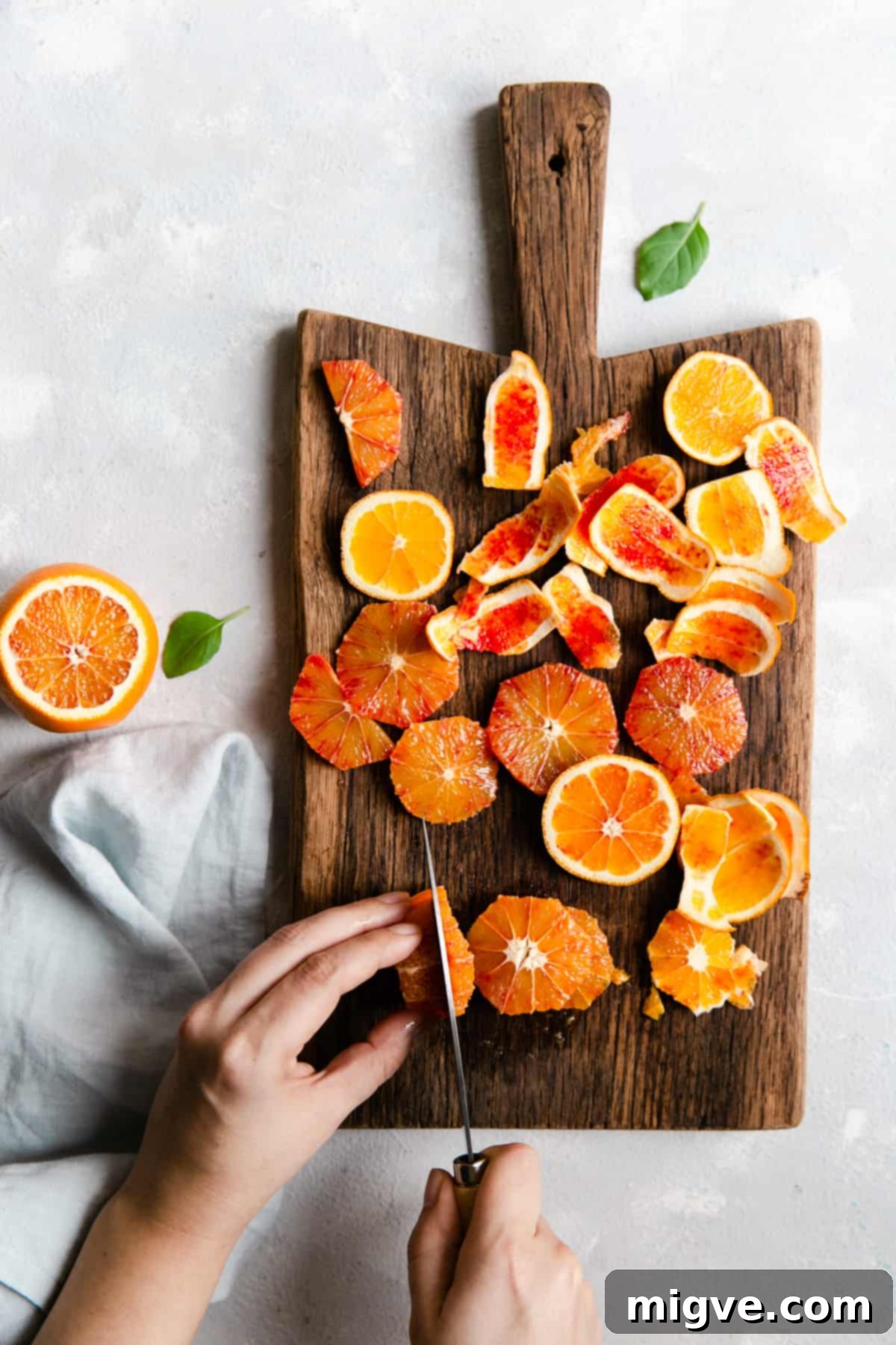 Overhead shot of a person carefully slicing a vibrant blood orange on a wooden chopping board