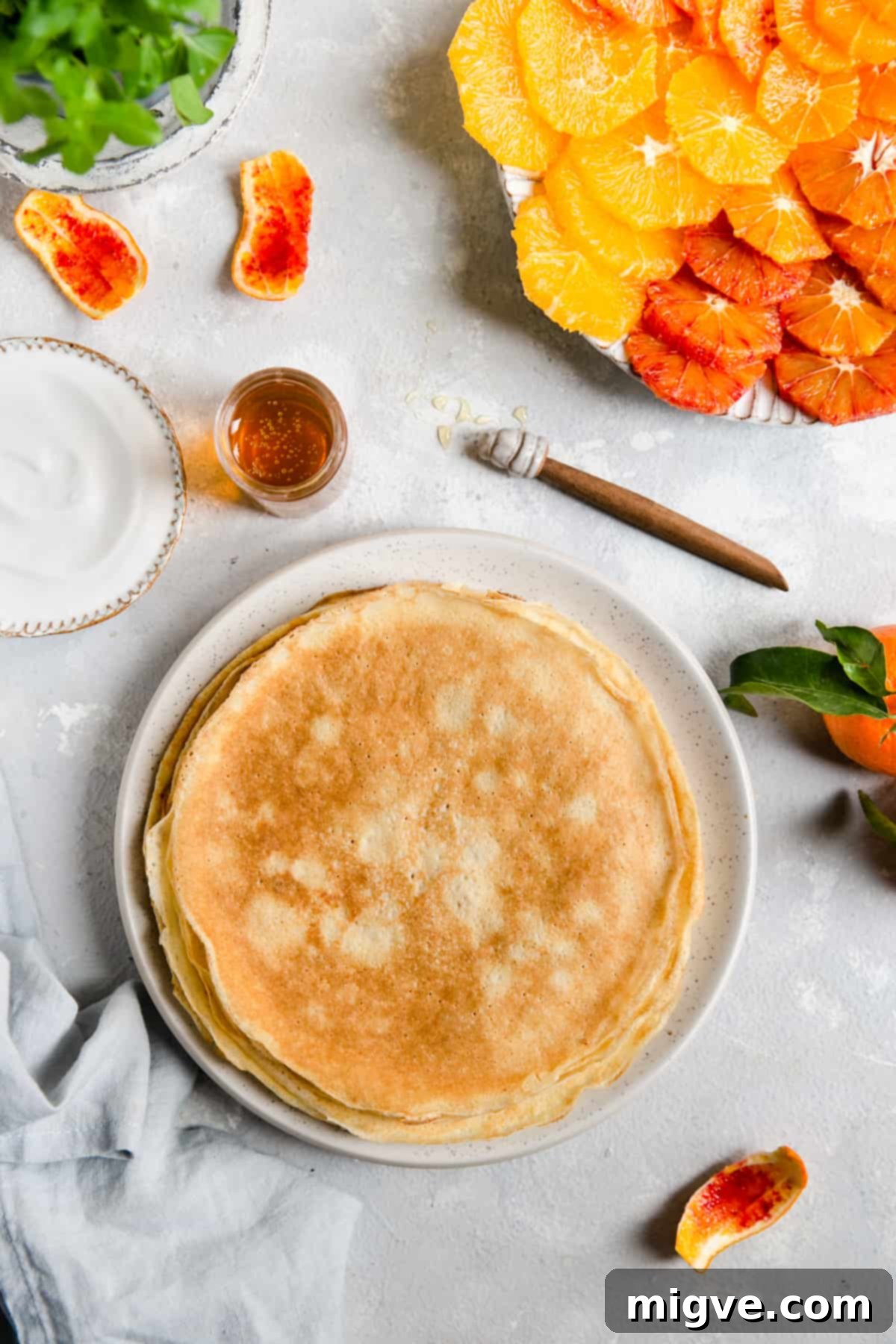 Overhead shot of a plate with neatly folded plain crepes alongside a small dish of vibrant citrus slices